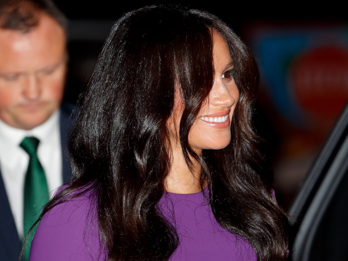 Meghan Markle, who body language expert Judi James said appeared to do a 'barrier ritual' in 2019 while royals aren't supposed to do barrier rituals including crossing their arms in public, smiles wearing a purple dress