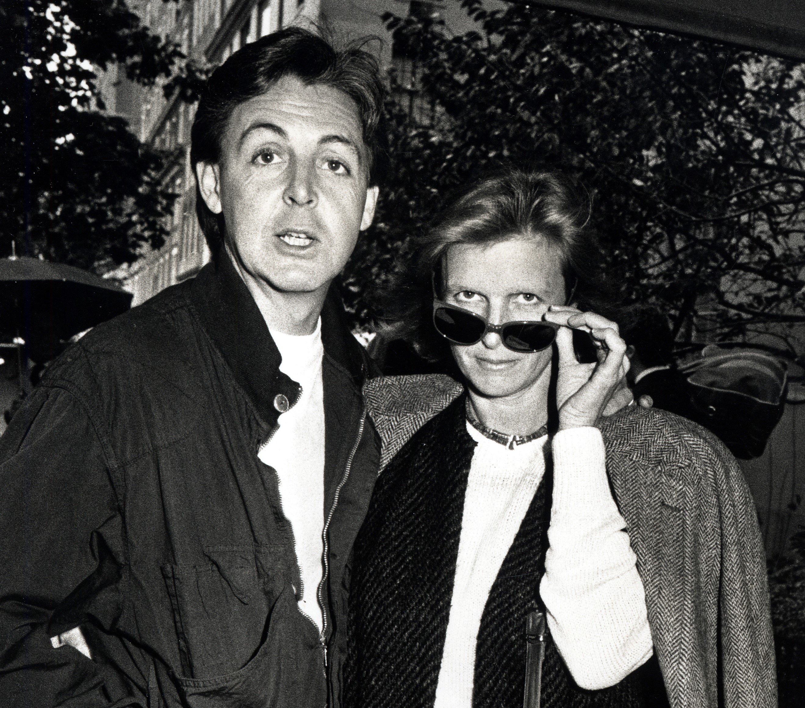 A black and white picture of Paul McCartney and Linda McCartney standing in front of trees.