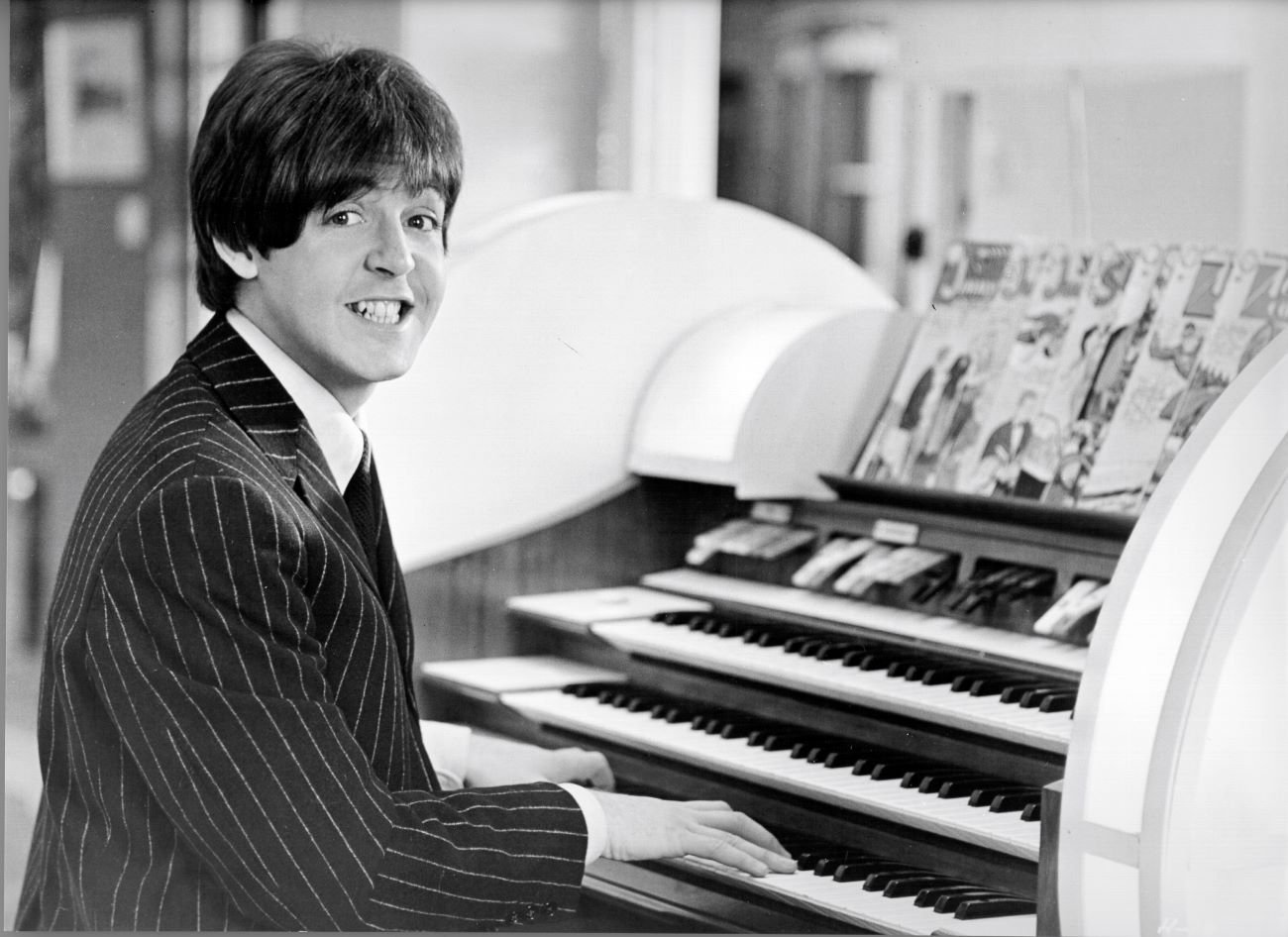 A black and white photo of Paul McCartney playing an organ. 
