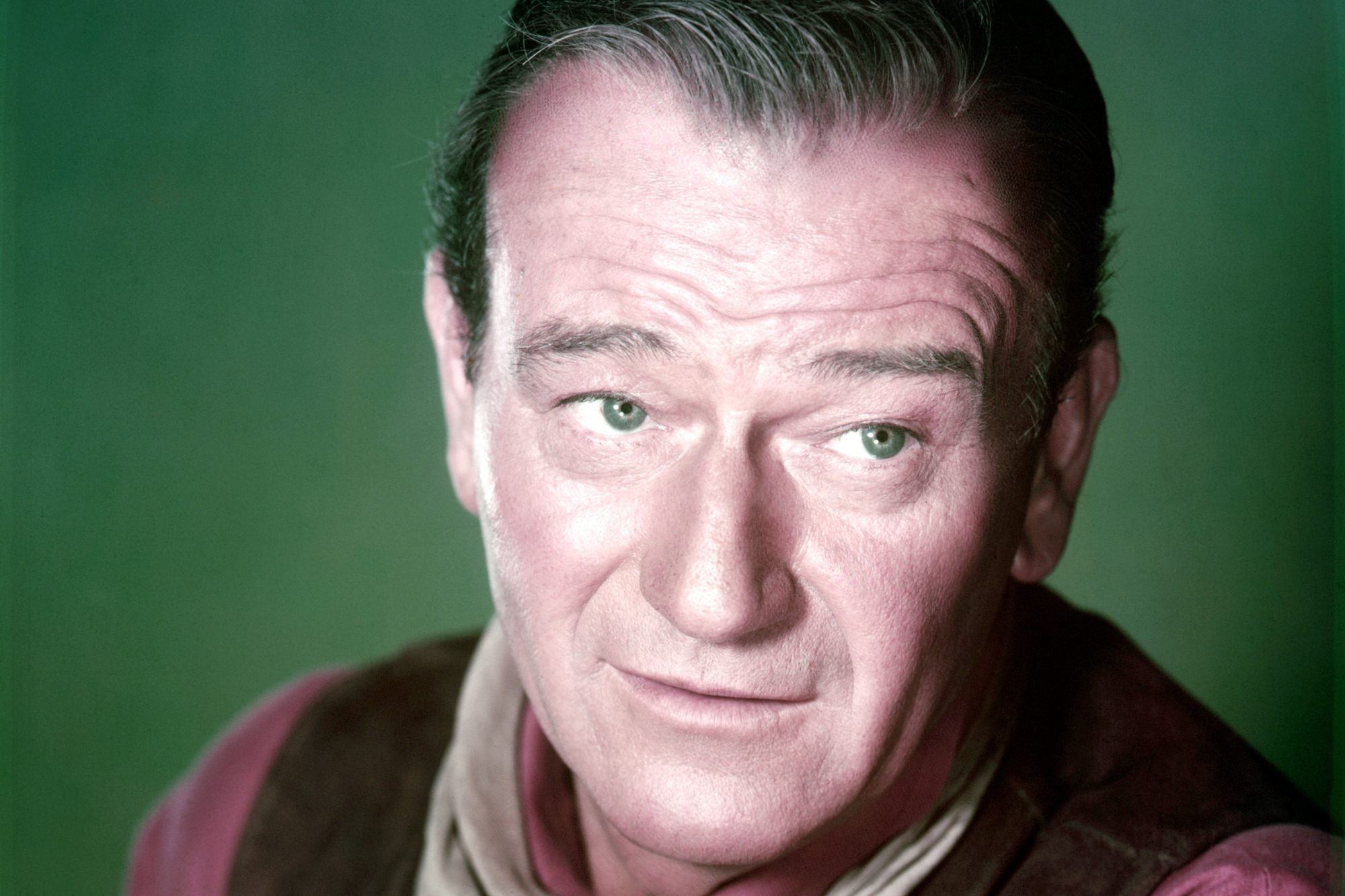Previous USC football player and movie star John Wayne wearing a Western costume looking to the side in front of a green background