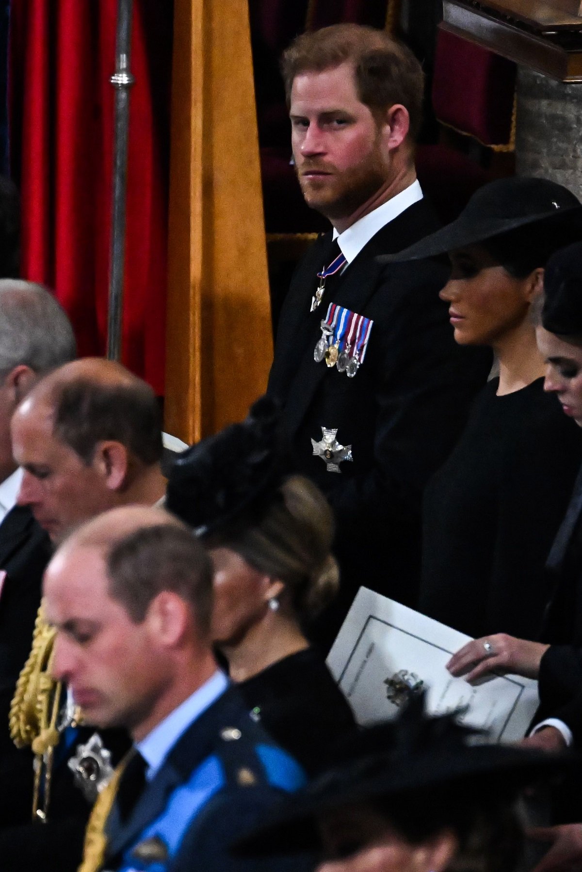 Prince Harry glaring at the camera in the second pew next to Meghan and behind working royals at Queen Elizabeth II's funeral