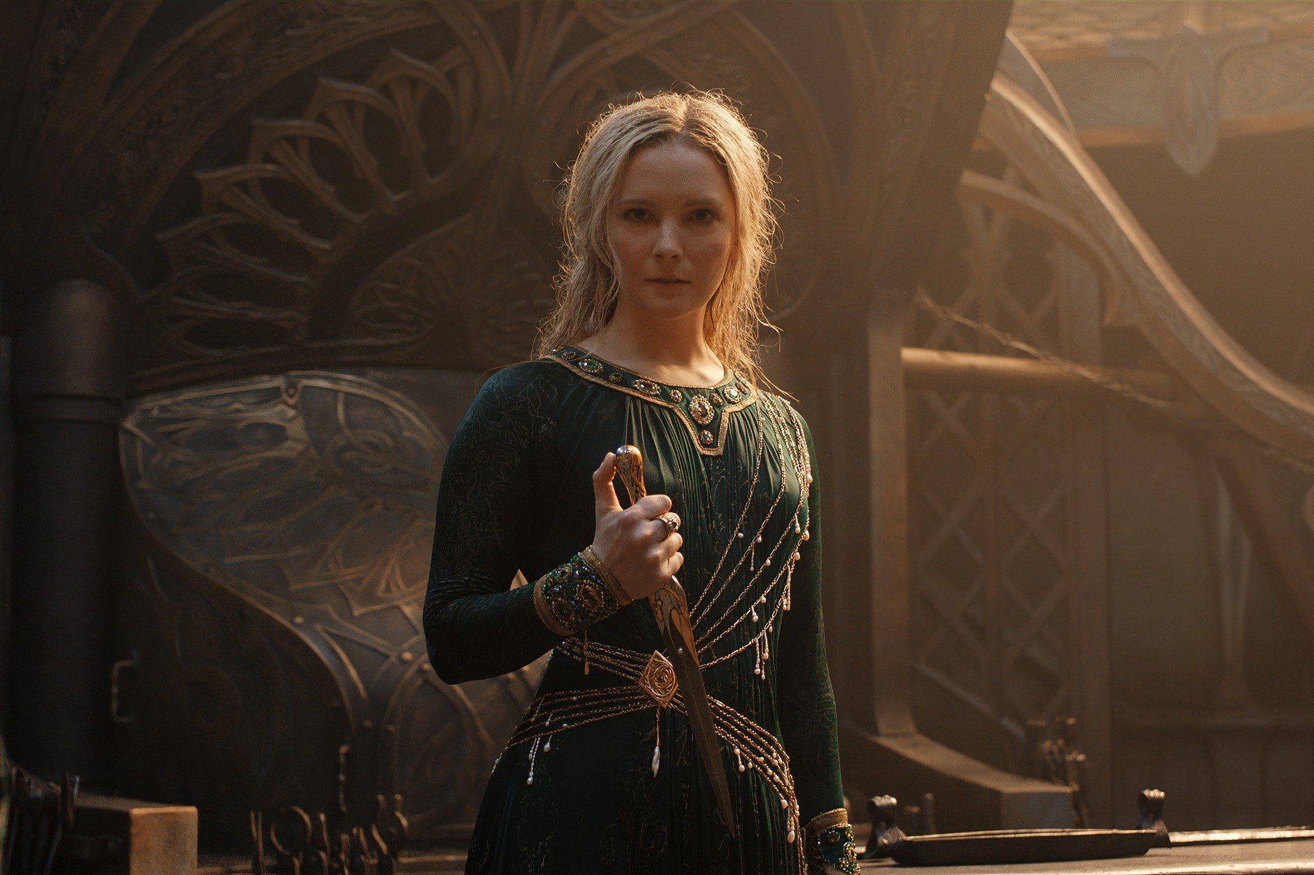 Morfydd Clark as Galadriel in 'The Rings of Power' Episode 8 for our article about its Easter Eggs. She's holding a blade and looks cautious.
