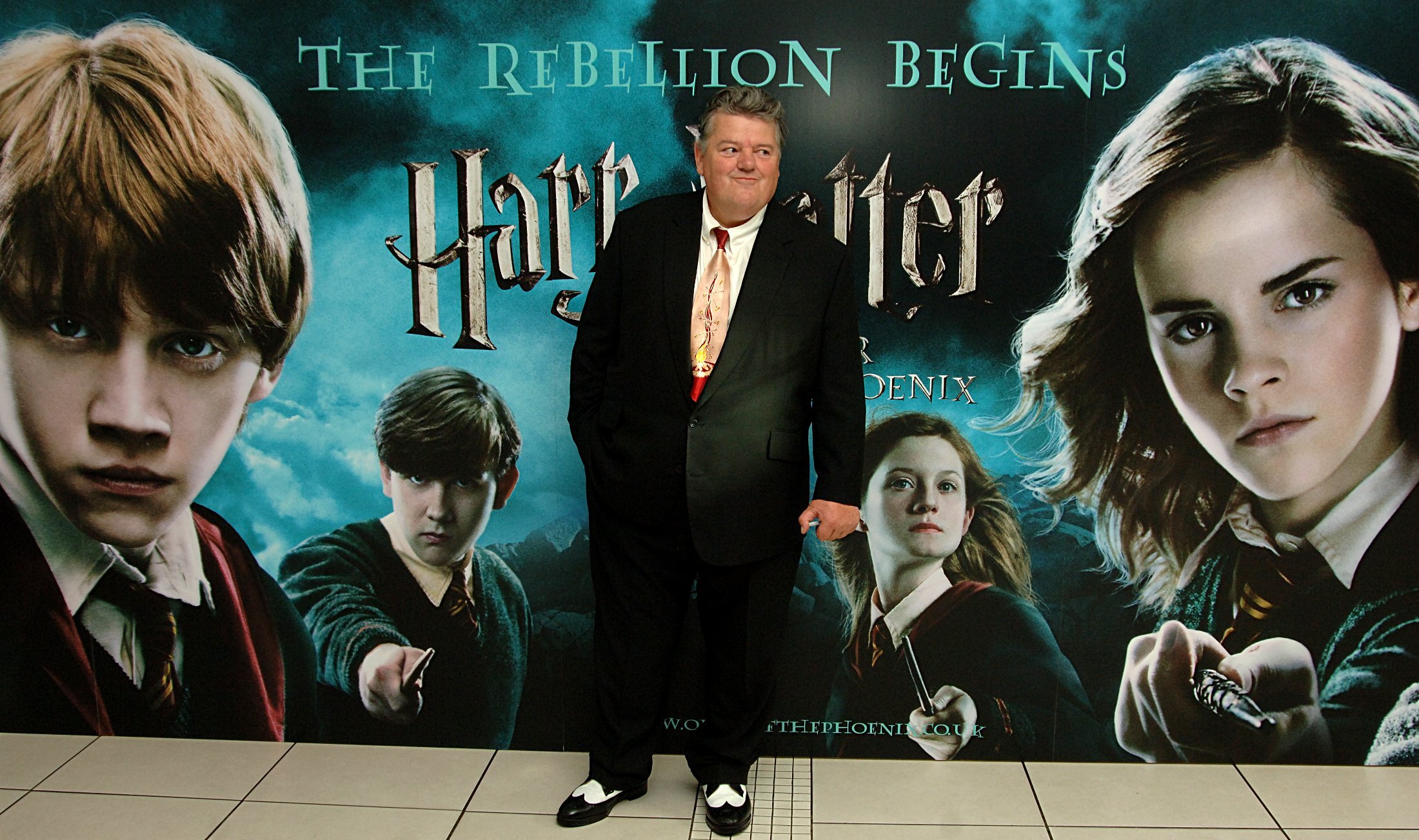 Robbie Coltrane poses in front of a Harry Potter poster.