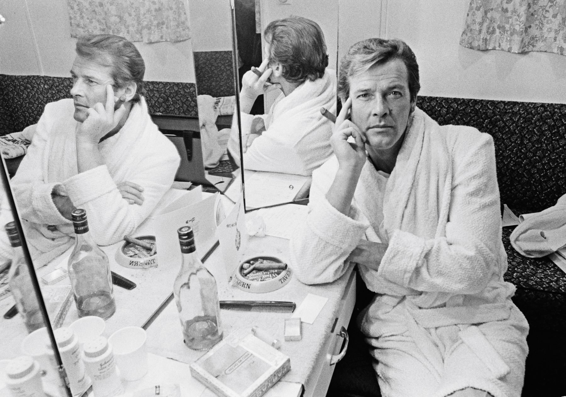 James Bond actor Roger Moore smoking a cigar in his dressing room while filming 'The Man with the Golden Gun'