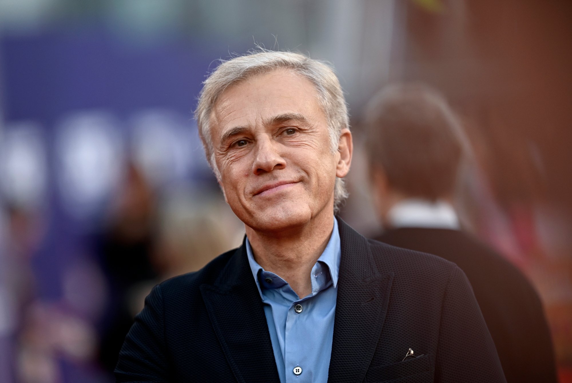 'Saturday Night Live' host Christoph Waltz with a slight smile. He's wearing a jacket and a blue dress shirt underneath.