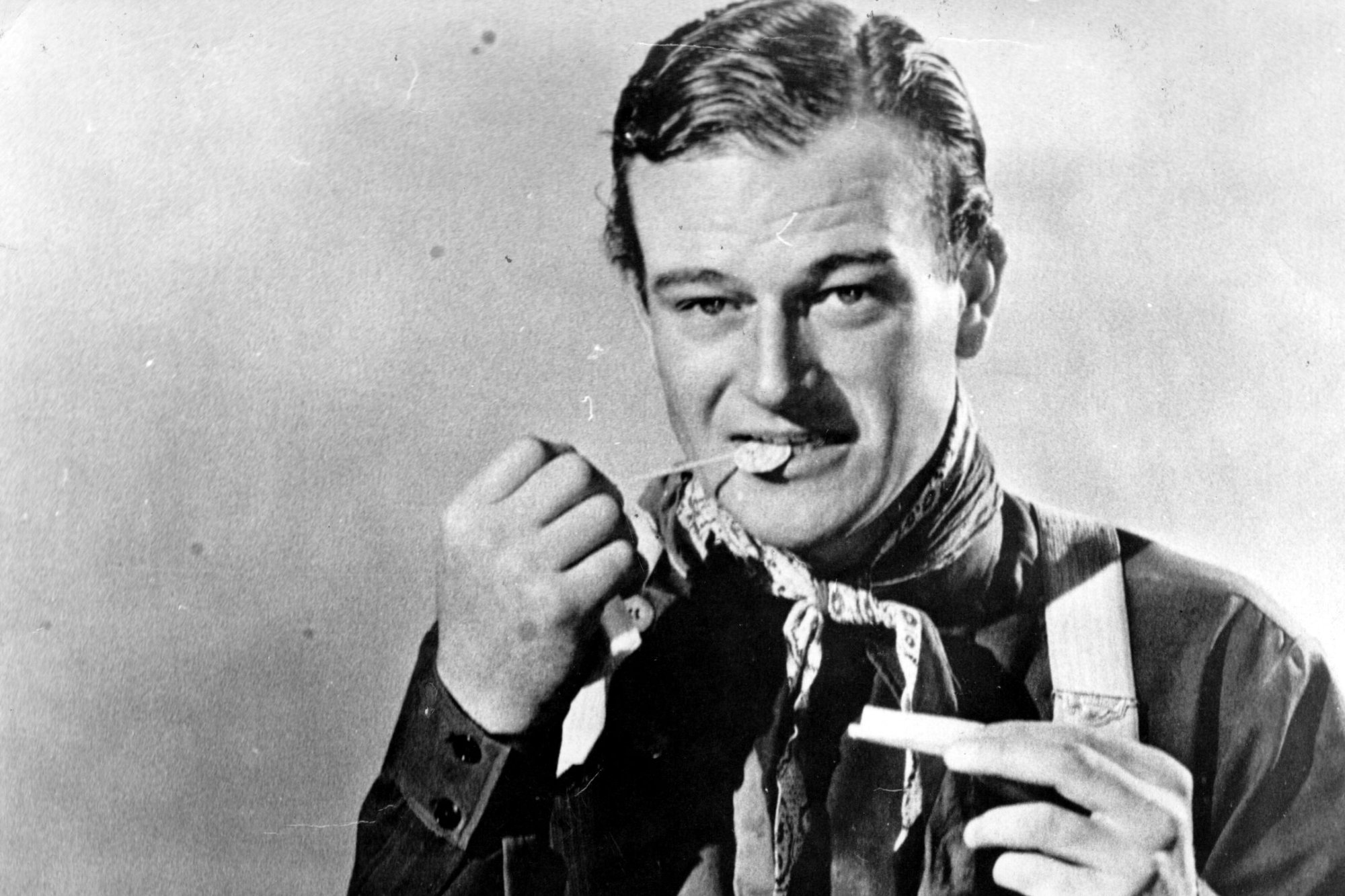 'Stagecoach' actor John Wayne, whose diet changed over time. He's holding a sphere object in his mouth and wearing a Western costume in a black-and-white picture.