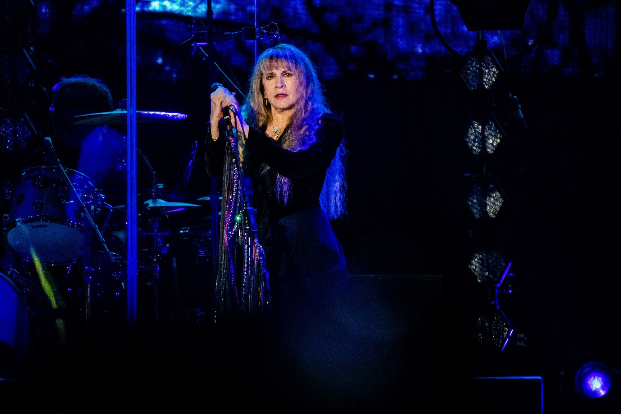 Stevie Nicks stands on stage and holds a microphone stand