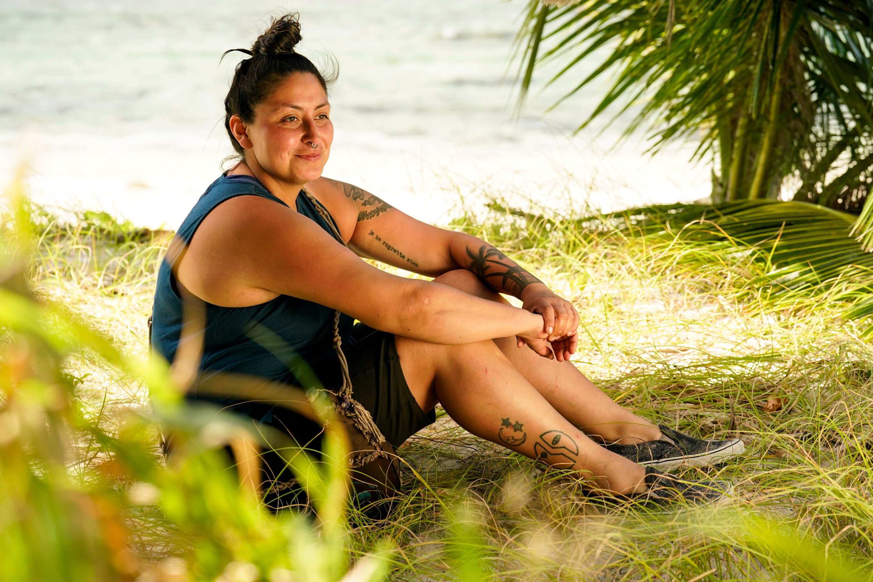 Karla Cruz Godoy, who has an immunity idol going into the merge in 'Survivor' Season 43 Episode 6, sits on the beach wearing a teal tank top and black shorts.