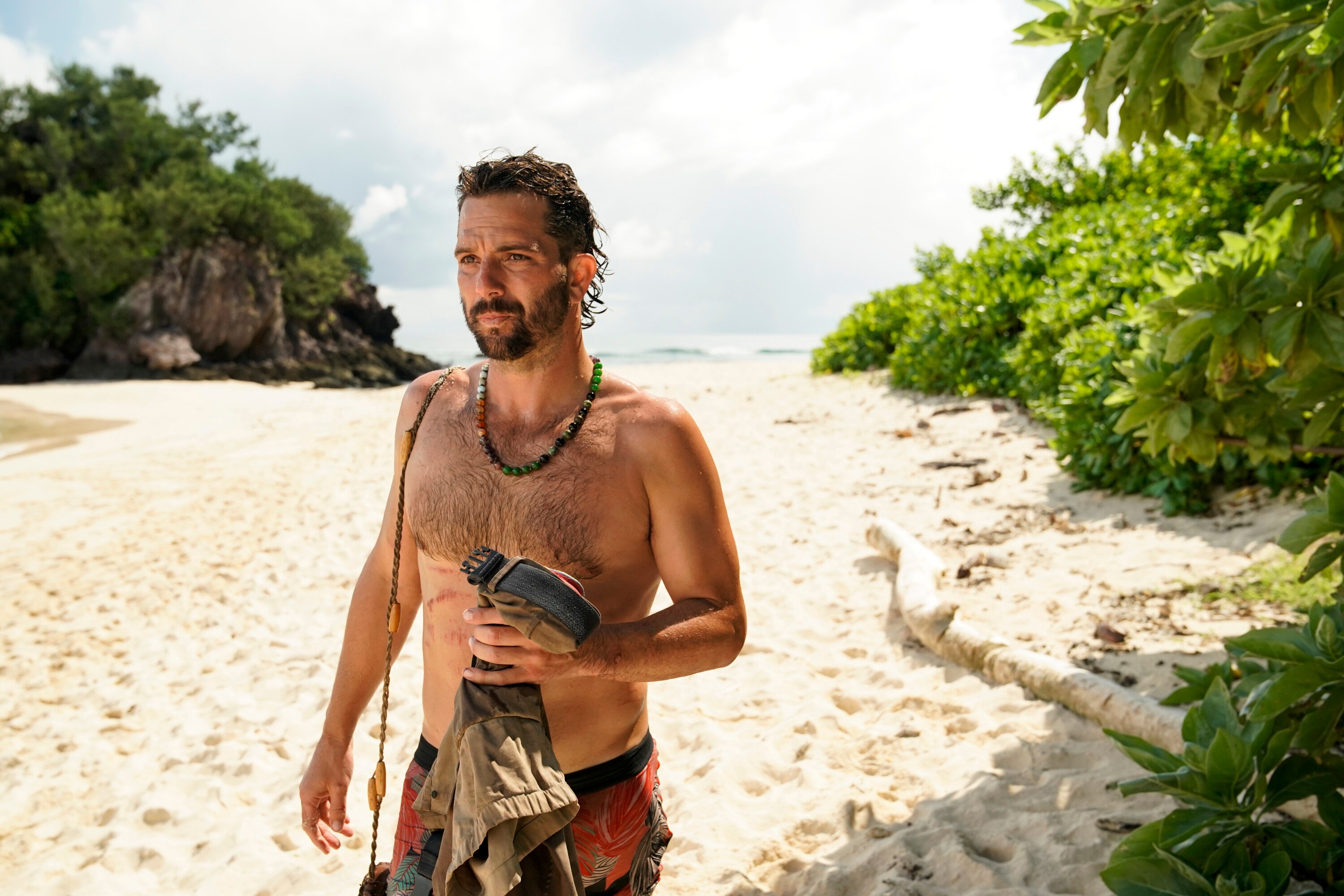 Cody Assenmacher, who is still in the running to be the 'Survivor' Season 43 winner, walks on the beach wearing red and black underwear and a beaded necklace.