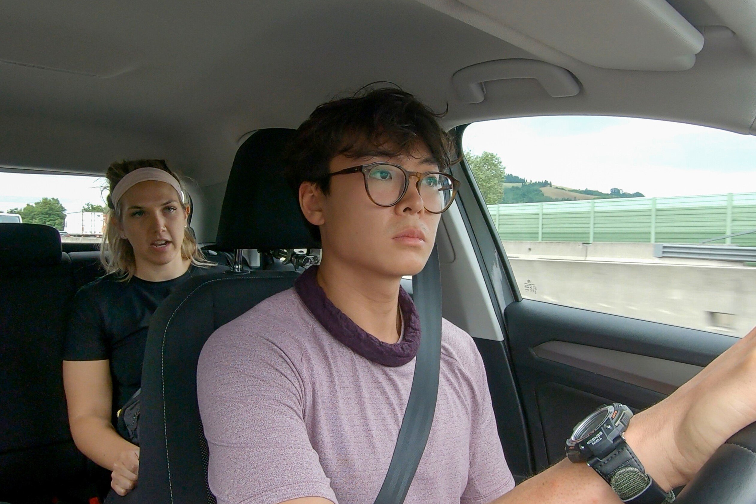 Claire Rehfuss and Derek Xiao, who star in 'The Amazing Race' Season 34, sit in a car with Derek in the driver's seat and Claire in the seat behind him.