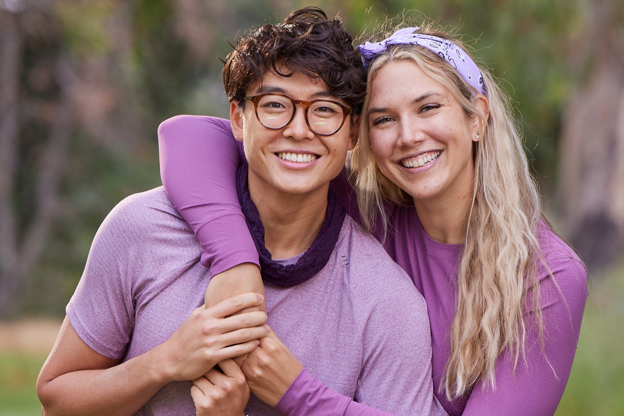 Derek Xiao and Claire Rehfuss, who, according to 'The Amazing Race' Season 34 spoilers, make it far in the competition, pose for promotional photos for the series. Derek wears a light purple shirt, a dark purple headband around his neck, and glasses. Claire wears a purple long-sleeved shirt and a light purple bandana.