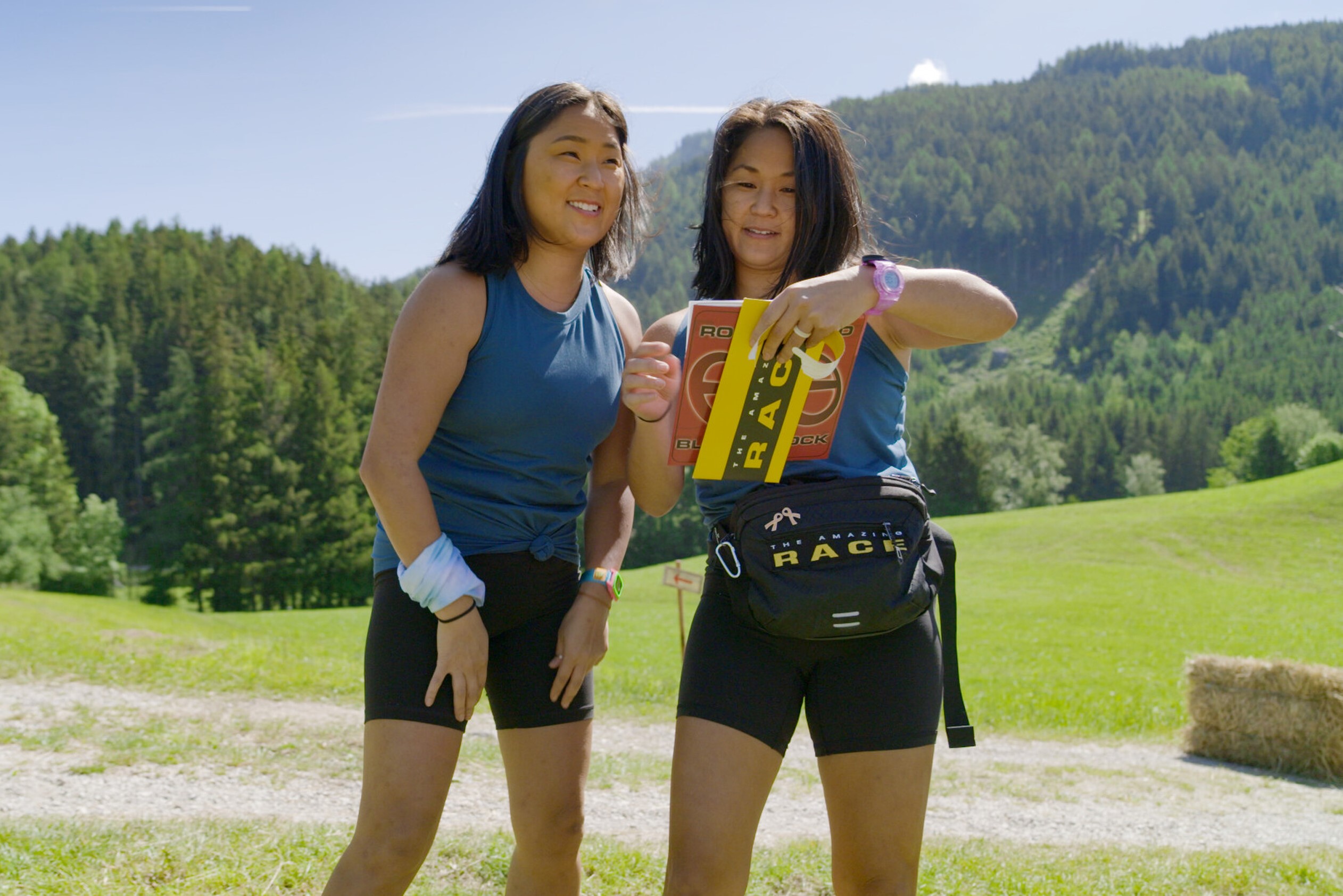 Emily Bushnell and Molly Sinert, who star in 'The Amazing Race' Season 34, which foregoes a historic twist, read a clue. The twins wear dark blue tank tops and black biker shorts.