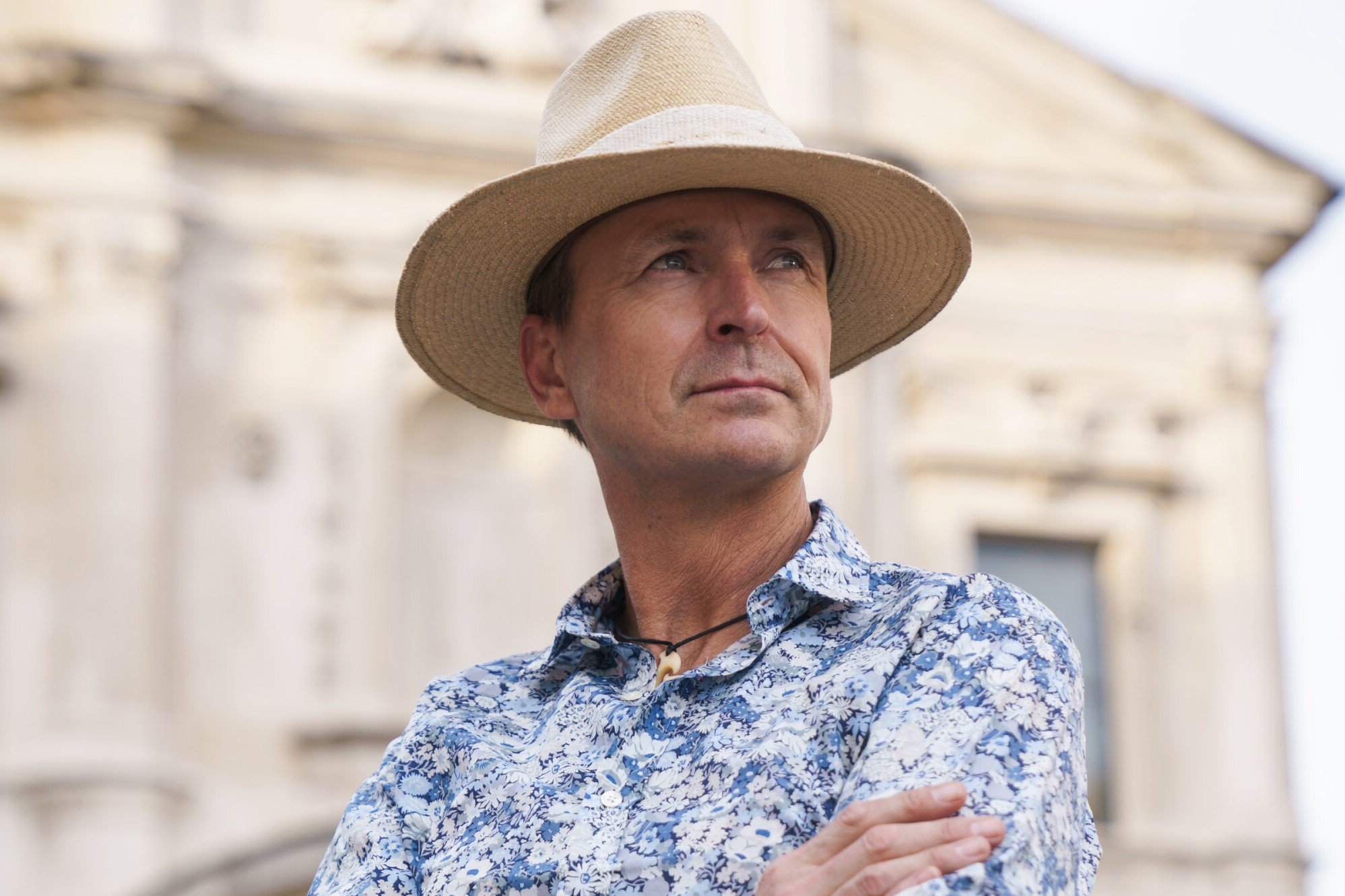Phil Keoghan, who hosts 'The Amazing Race' Season 34 on CBS, wears a blue floral print button-up long-sleeved shirt and beige hat.
