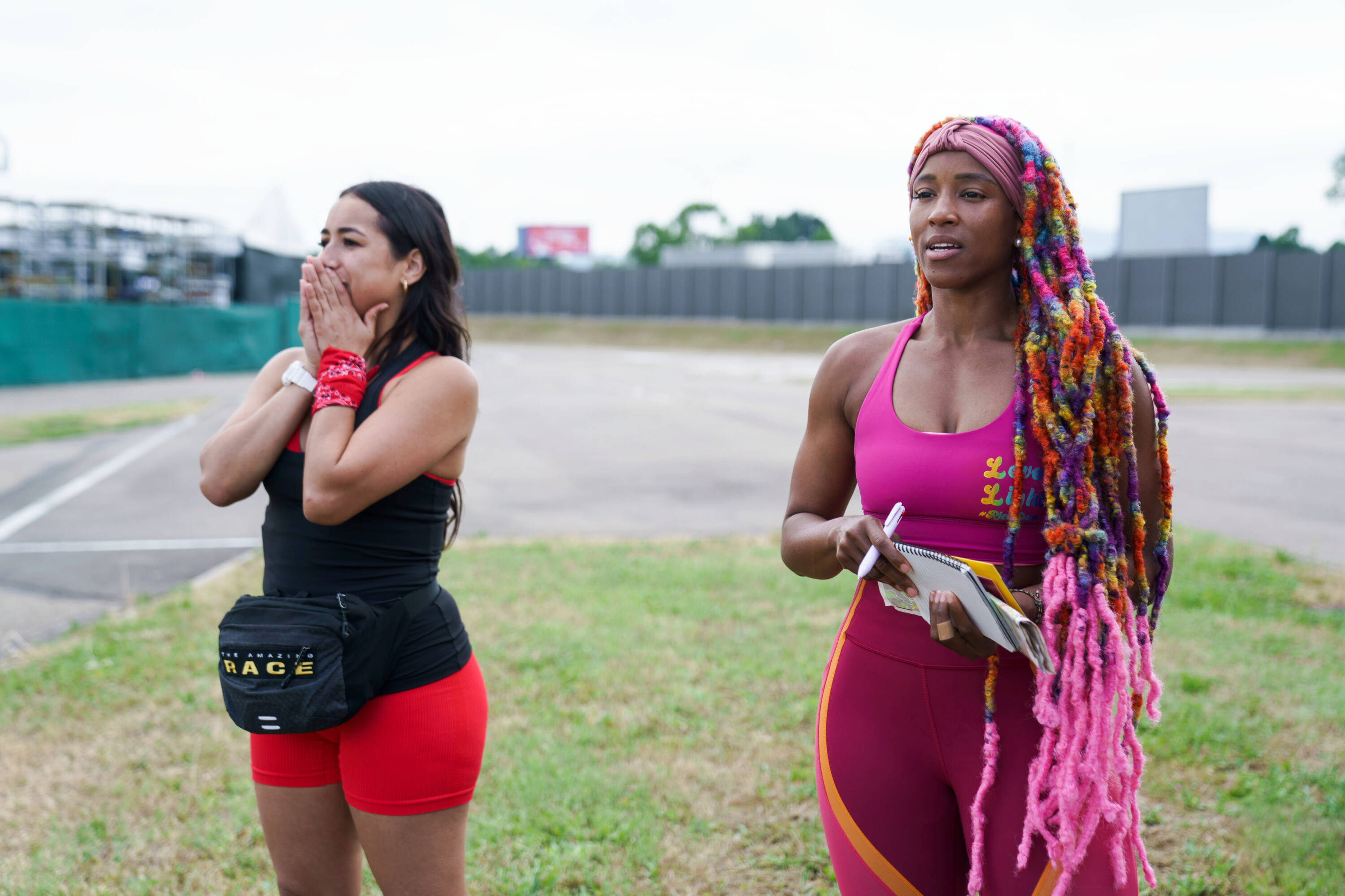 Michelle Burgos and Dom Jones, who star in 'The Amazing Race' Season 34 tonight, Oct. 5, on CBS, stand next to each other at a challenge. Michelle wears a black tank top and red shorts. Dom wears a pink sports bra and pink leggings.