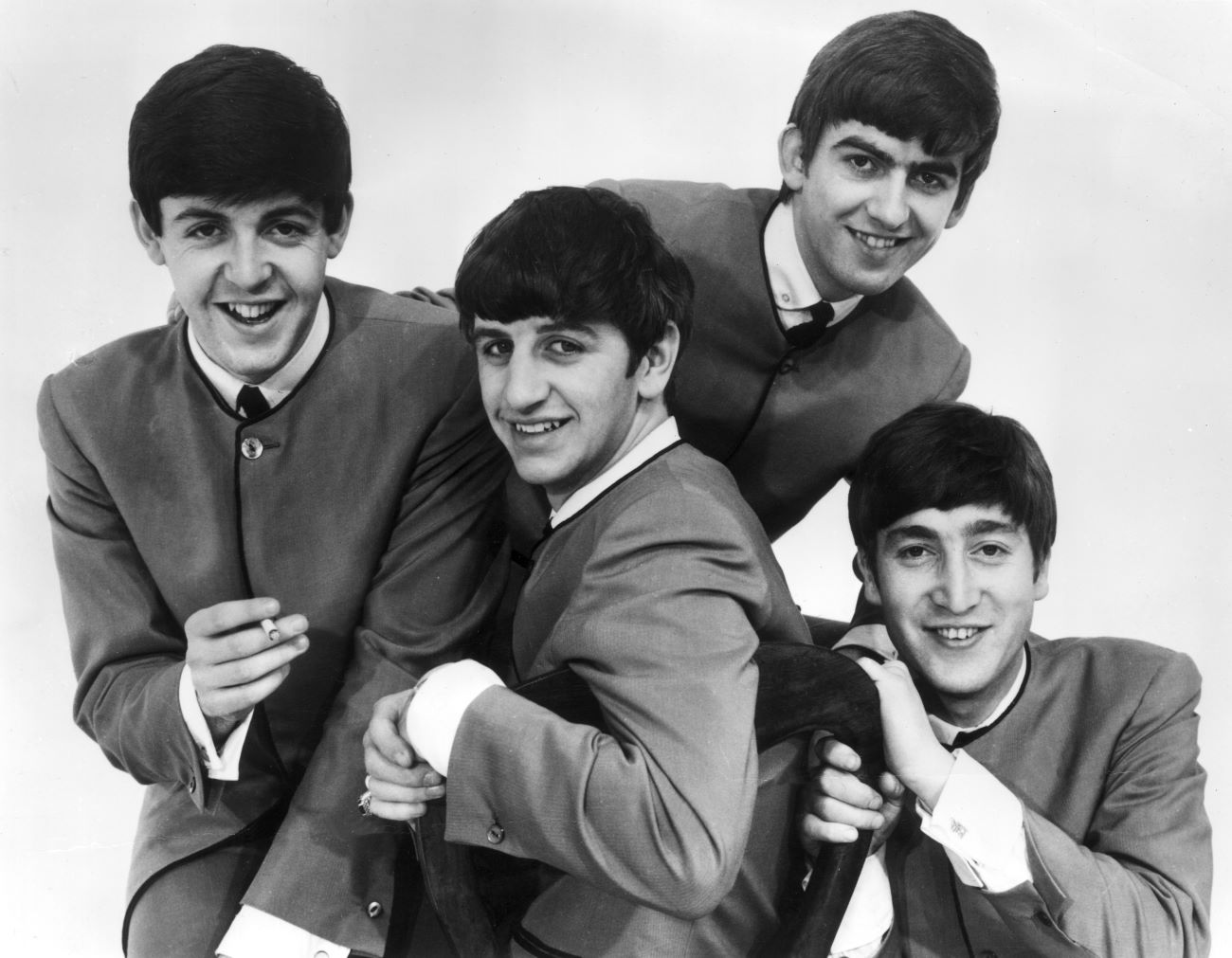 A black and white photo of Paul McCartney, Ringo Starr, George Harrison, and John Lennon of The Beatles wearing matching outfits. 