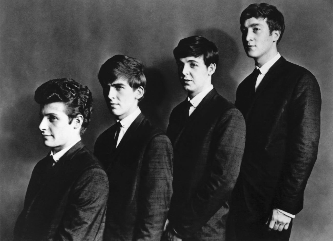 A black and white photo of Pete Best, George Harrison, Paul McCartney and John Lennon standing in an ascending line.