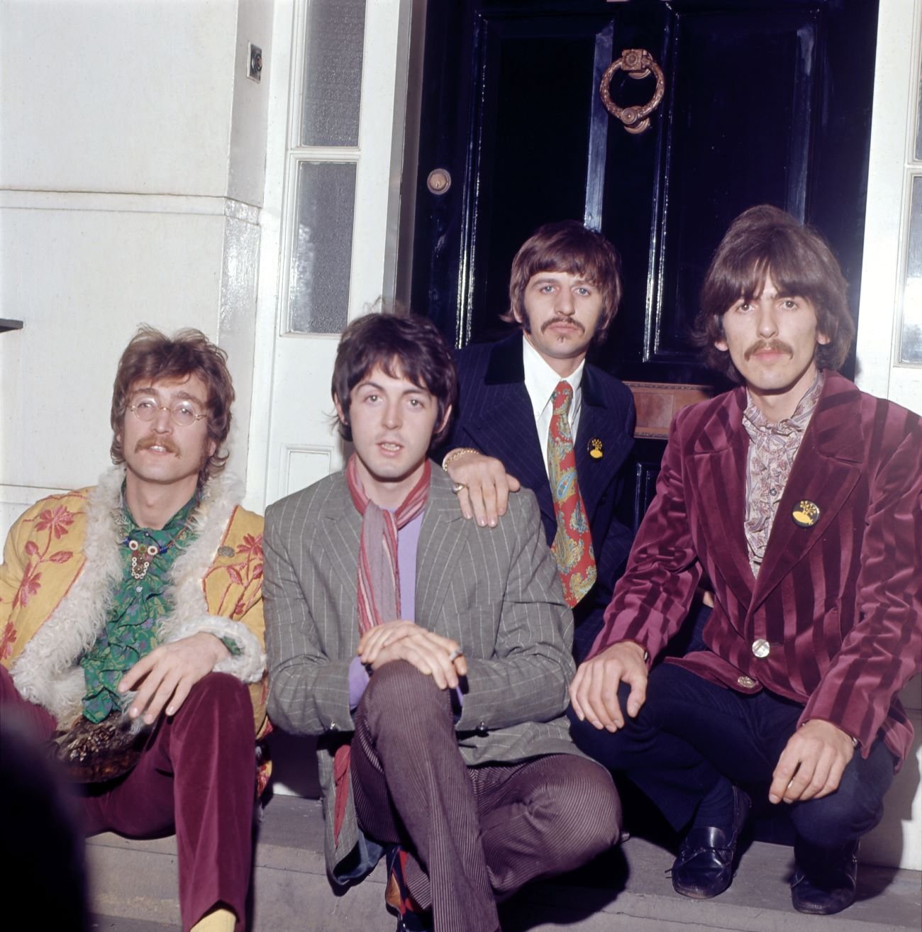The Beatles, John Lennon, Paul McCartney, Ringo Starr, and George Harrison, sit on a doorstep.