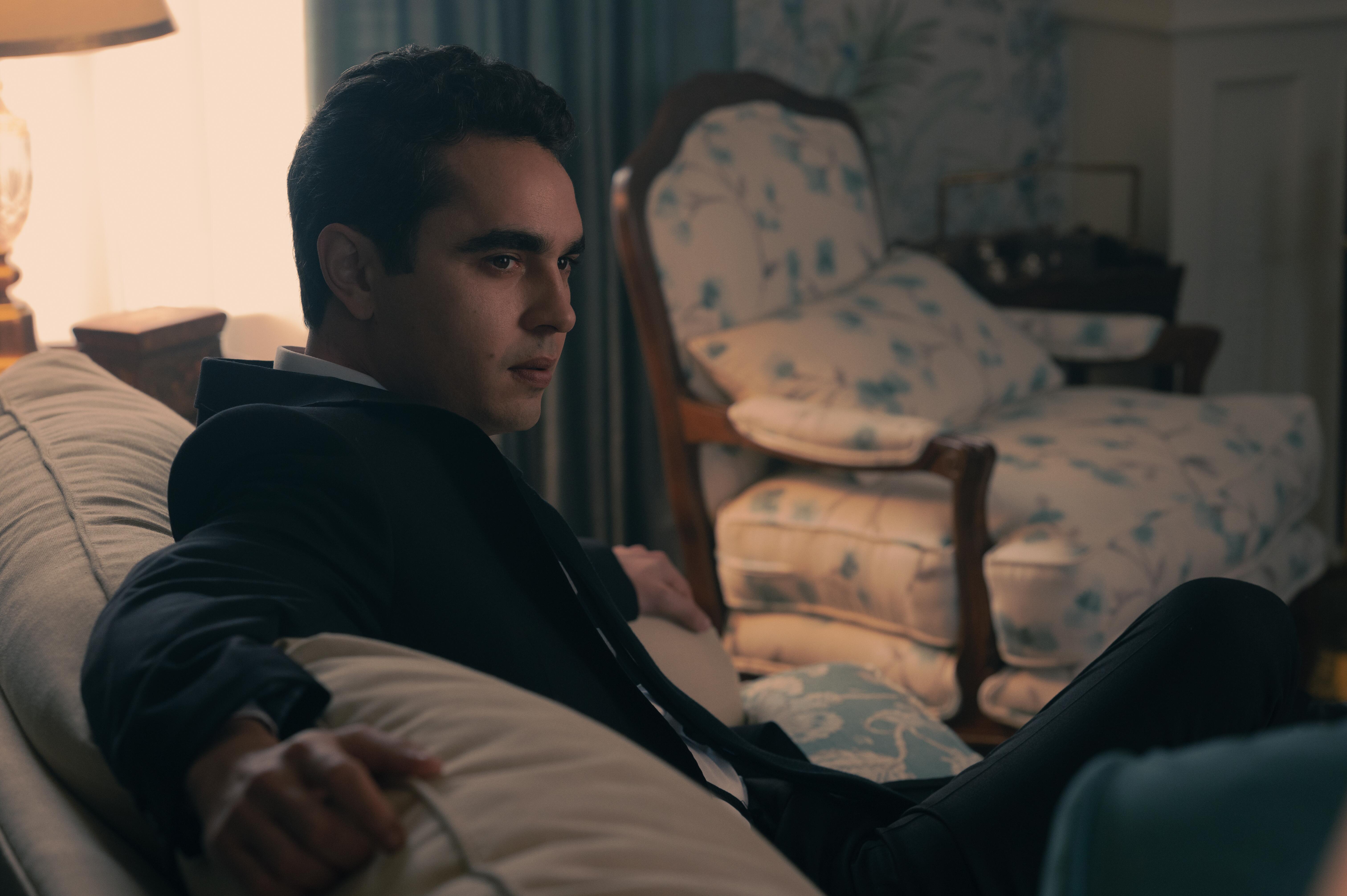 Nick Blaine sits on a couch with his arms outstretched in 'The Handmaid's Tale'