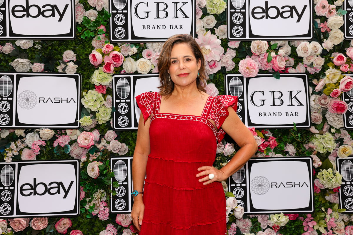 The Patient actor Laura Niemi wears a red dress and poses in front of a wall of flowers.