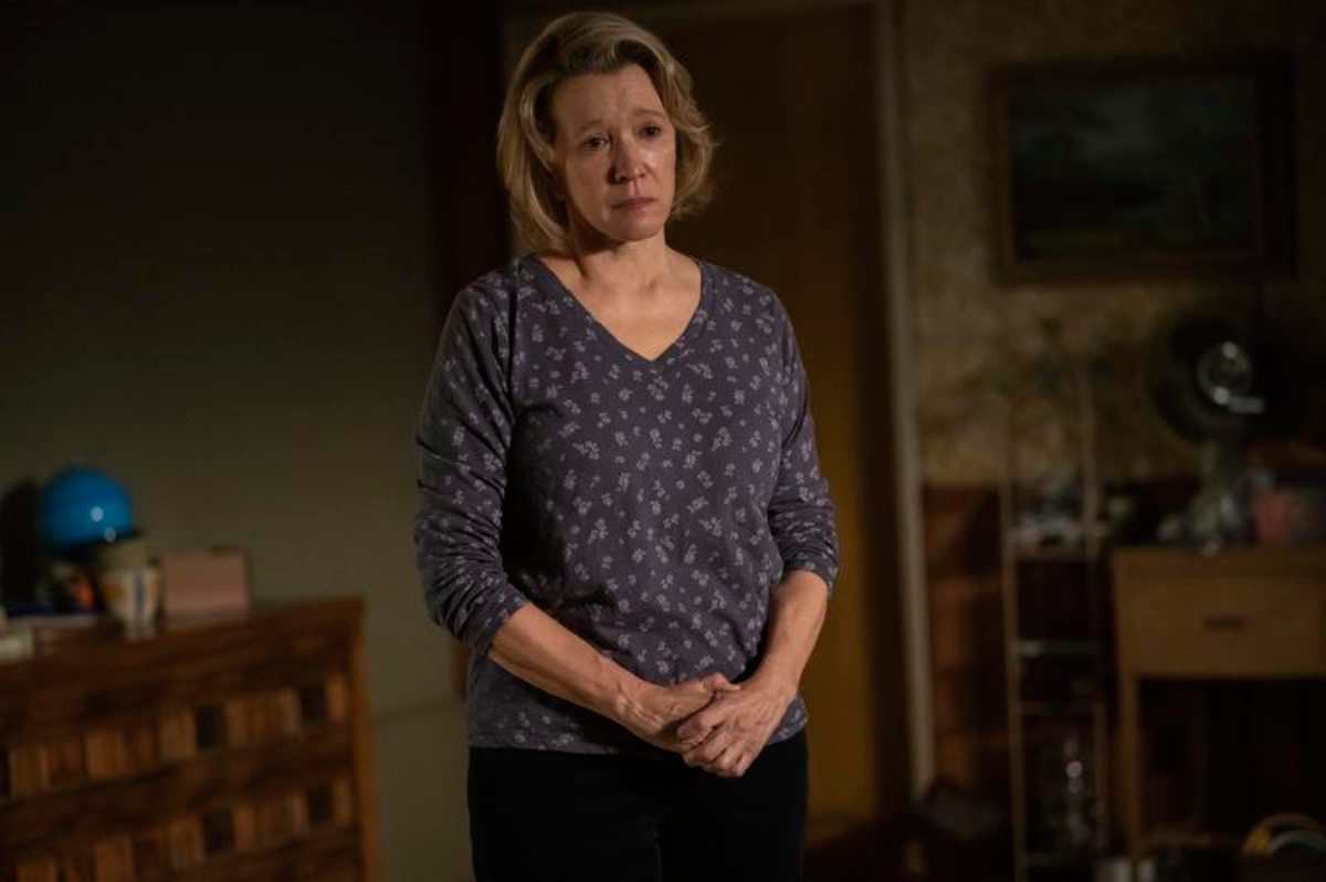 Linda Emond as Candace in Hulu's The Patient. Candace wears a purple top and stands in Sam's basement looking teary-eyed.