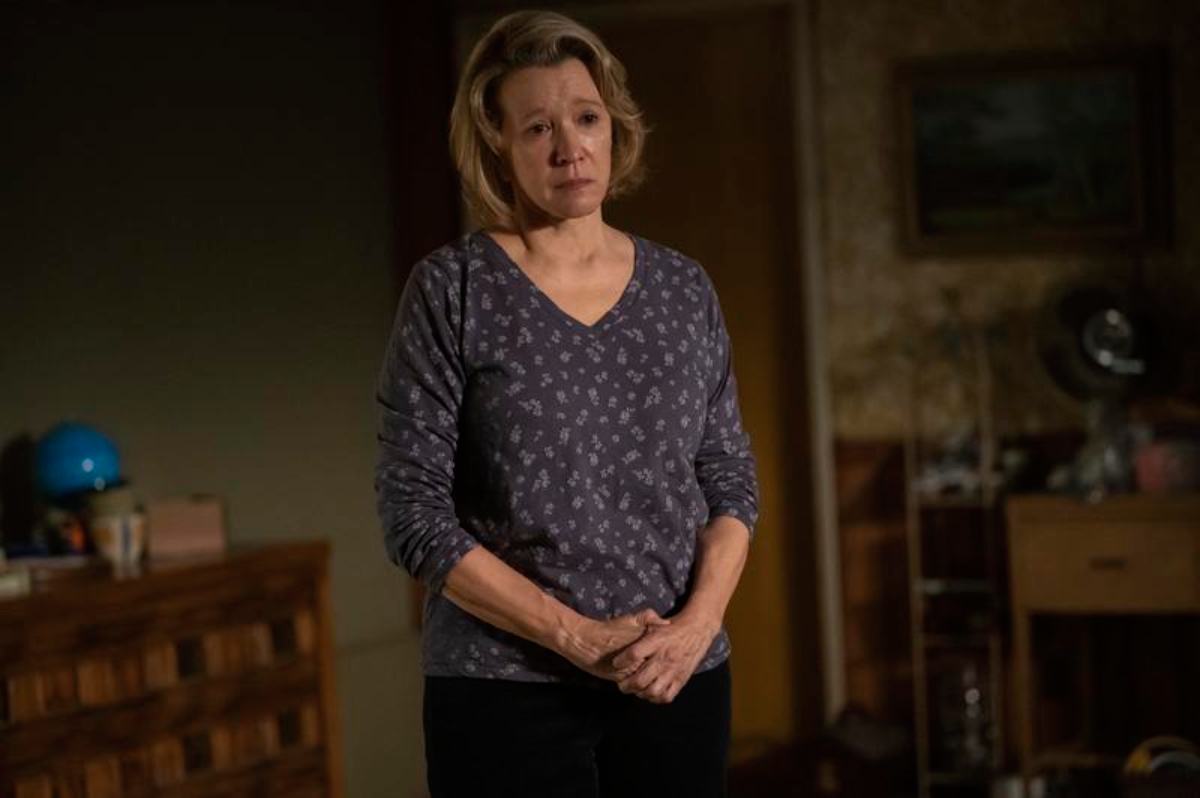 Linda Emond as Candace in Hulu's The Patient. Candace wears a purple top and stands in Sam's basement looking teary-eyed. 