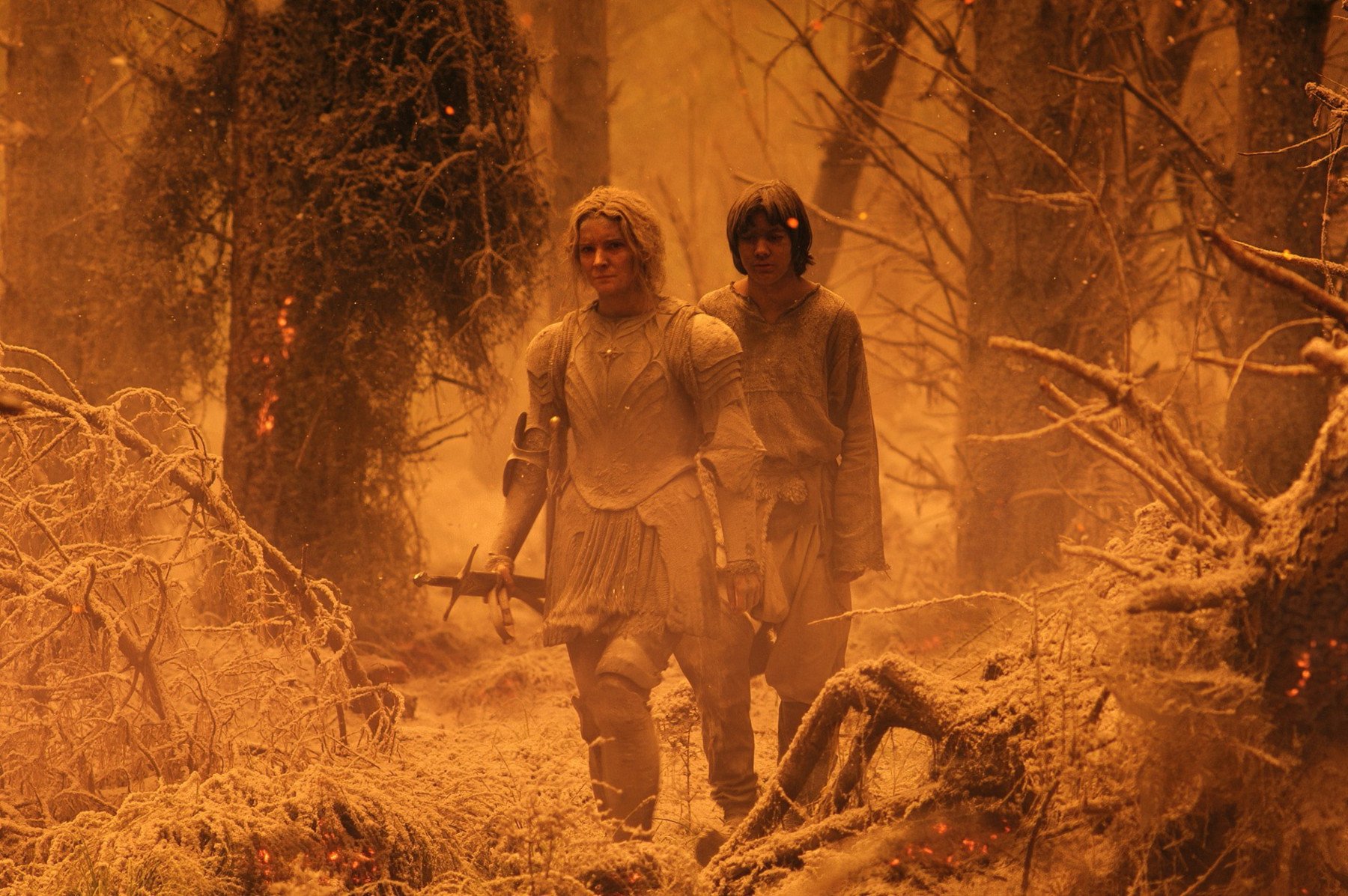 Morfydd Clark and Tyroe Muhafidin as Galadriel and Theo in 'The Rings of Power' Episode 7 for our article about its Easter Eggs. They're walking through the burned Southlands, and everything is orange and ashy.