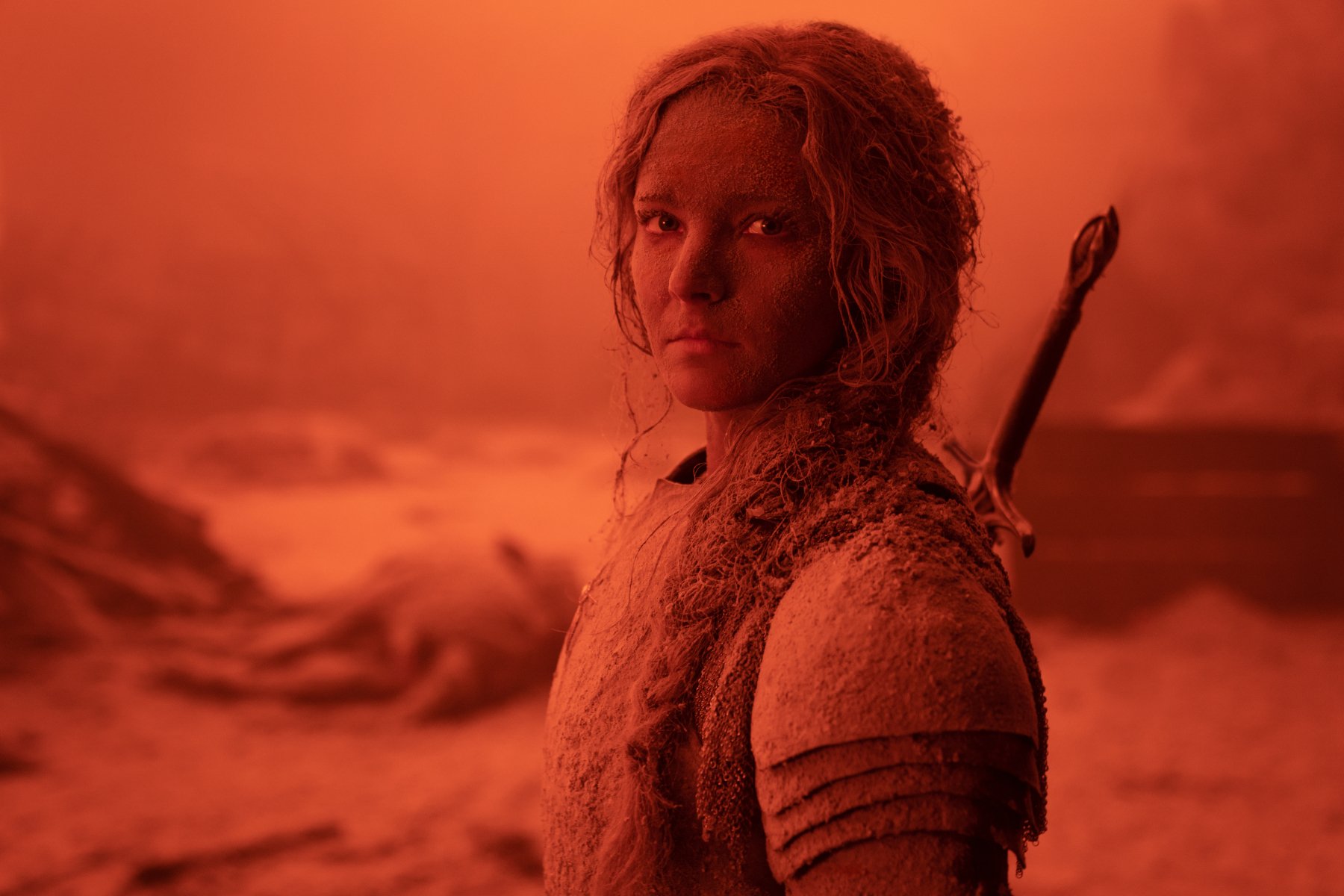 Morfydd Clark as Galadriel in 'The Rings of Power' Episode 7. She's standing in the destruction of the Southlands, everything is red, and she seems to be covered in ash.