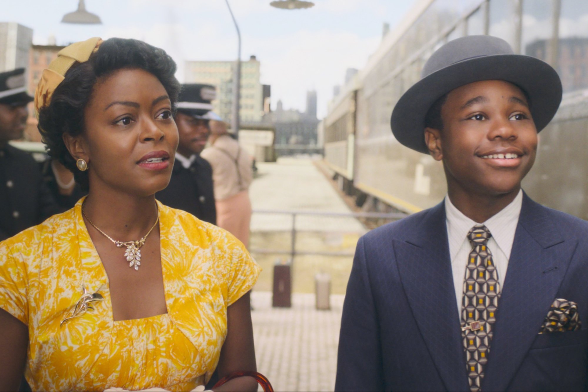 'Till' Danielle Deadwyler as Mamie Till-Mobley and Jalyn Hall as Emmett Till. Deadwyler is wearing a yellow and white dress and Hall is wearing a suit, tie, and a hat. They're standing outside of a train at the train station.