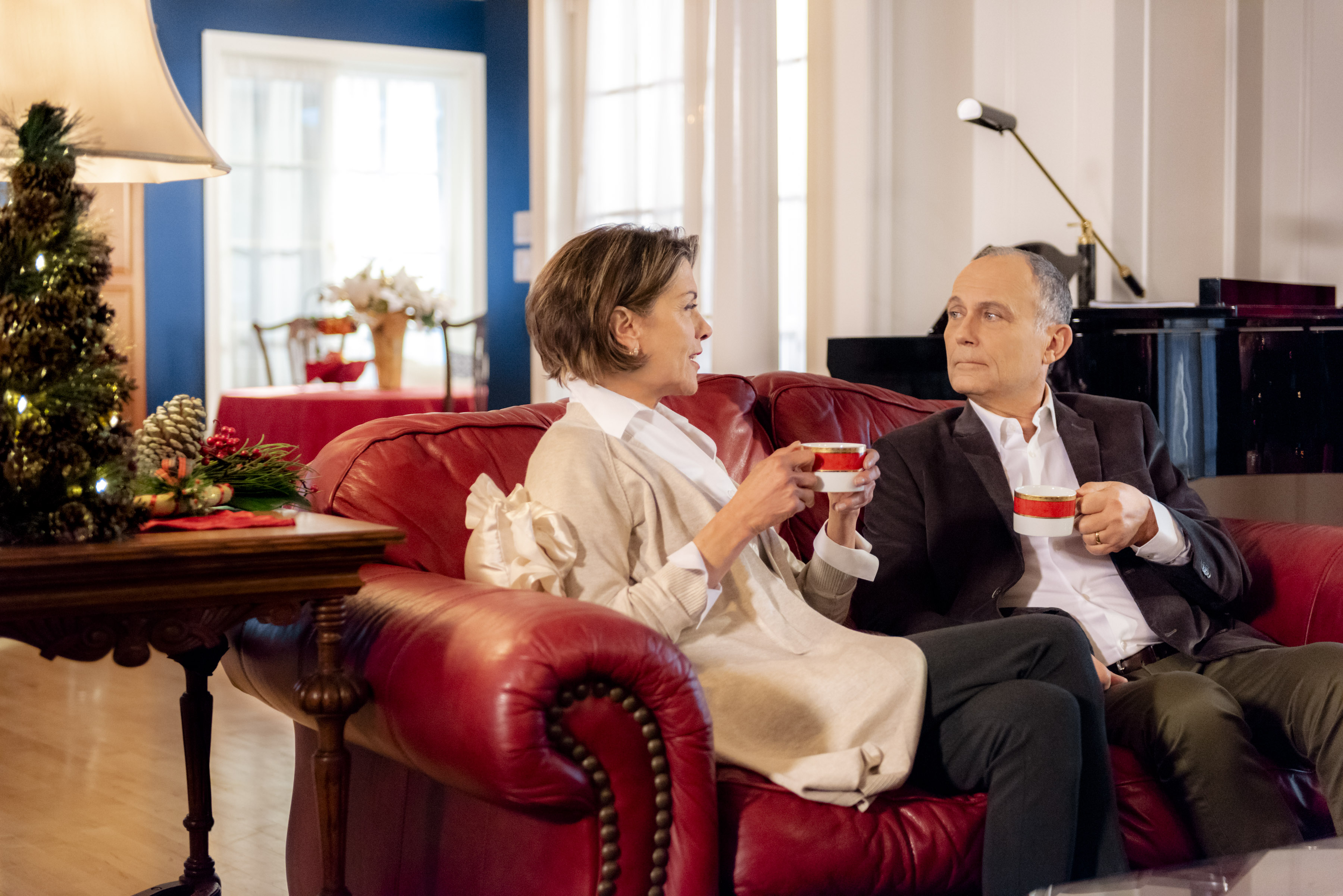 Wendie Malick and Michael Kopsa sitting on a couch in the Hallmark Channel movie 'Marrying Father Christmas'