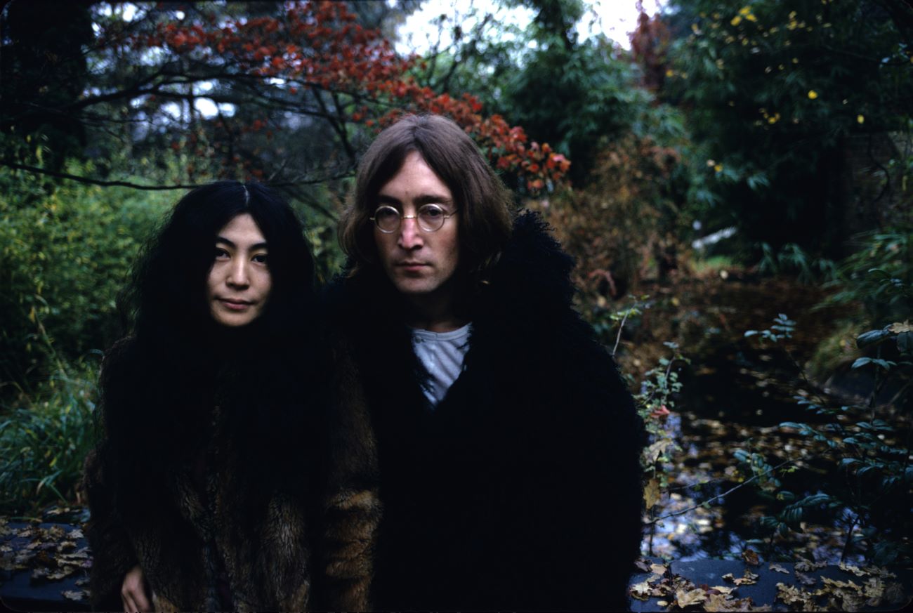 John Lennon and Yoko Ono pose in front of trees.