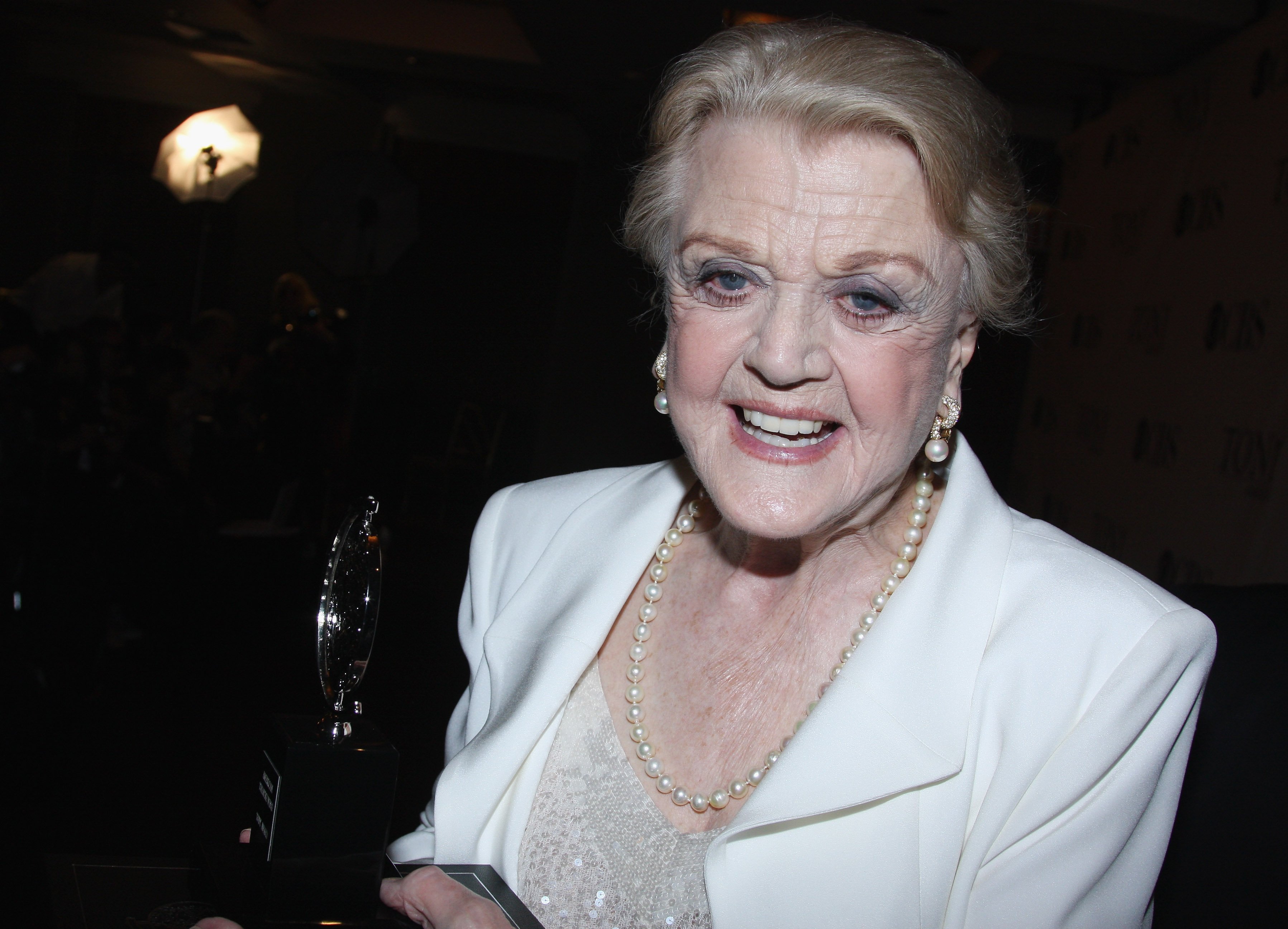 Angela Lansbury smiles and wears a white blazer with pearls to the 2009 Tony Awards at Radio City Musical Hall.