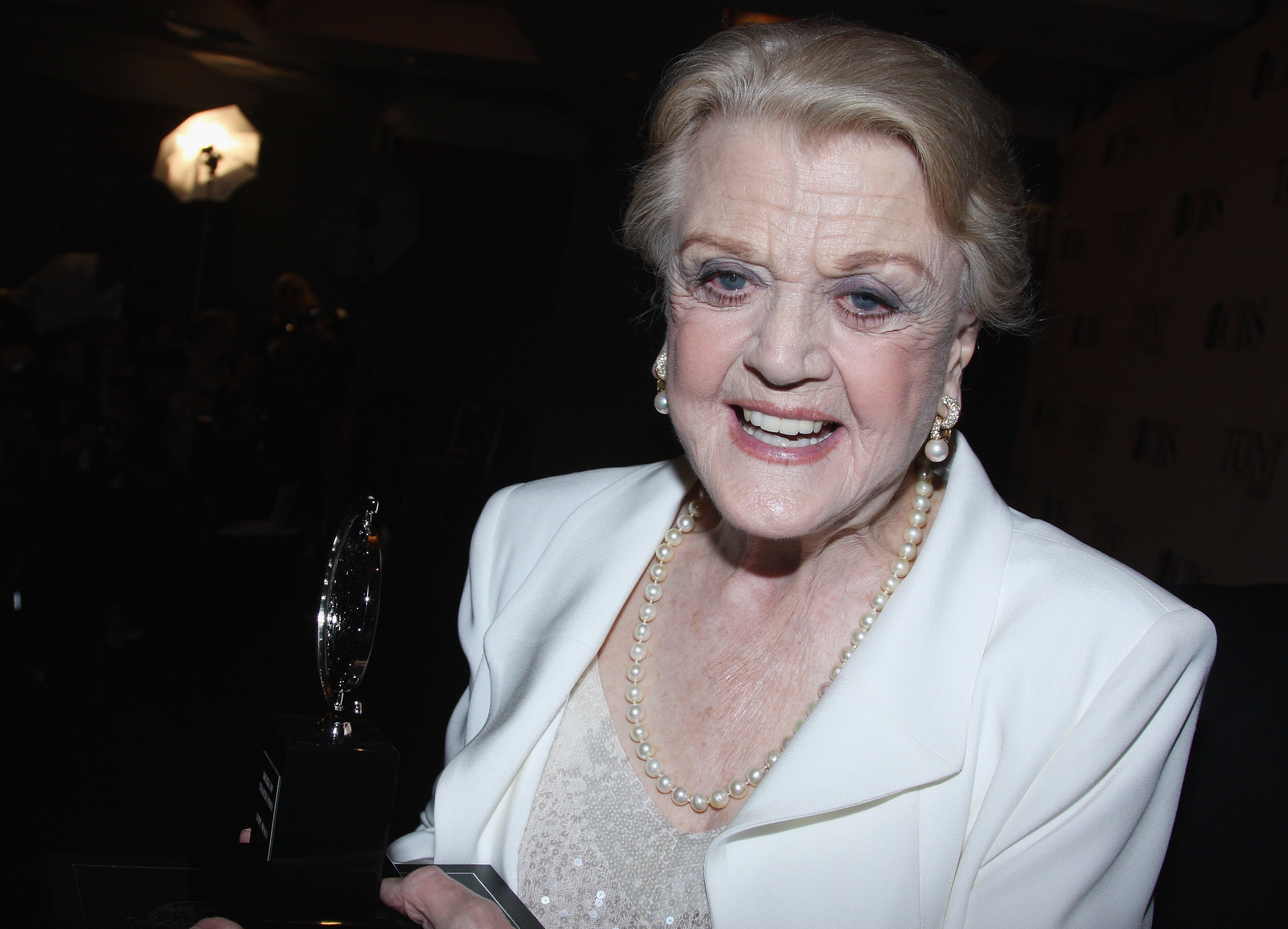Angela Lansbury smiles and wears a white blazer with pearls to the 2009 Tony Awards at Radio City Musical Hall. 