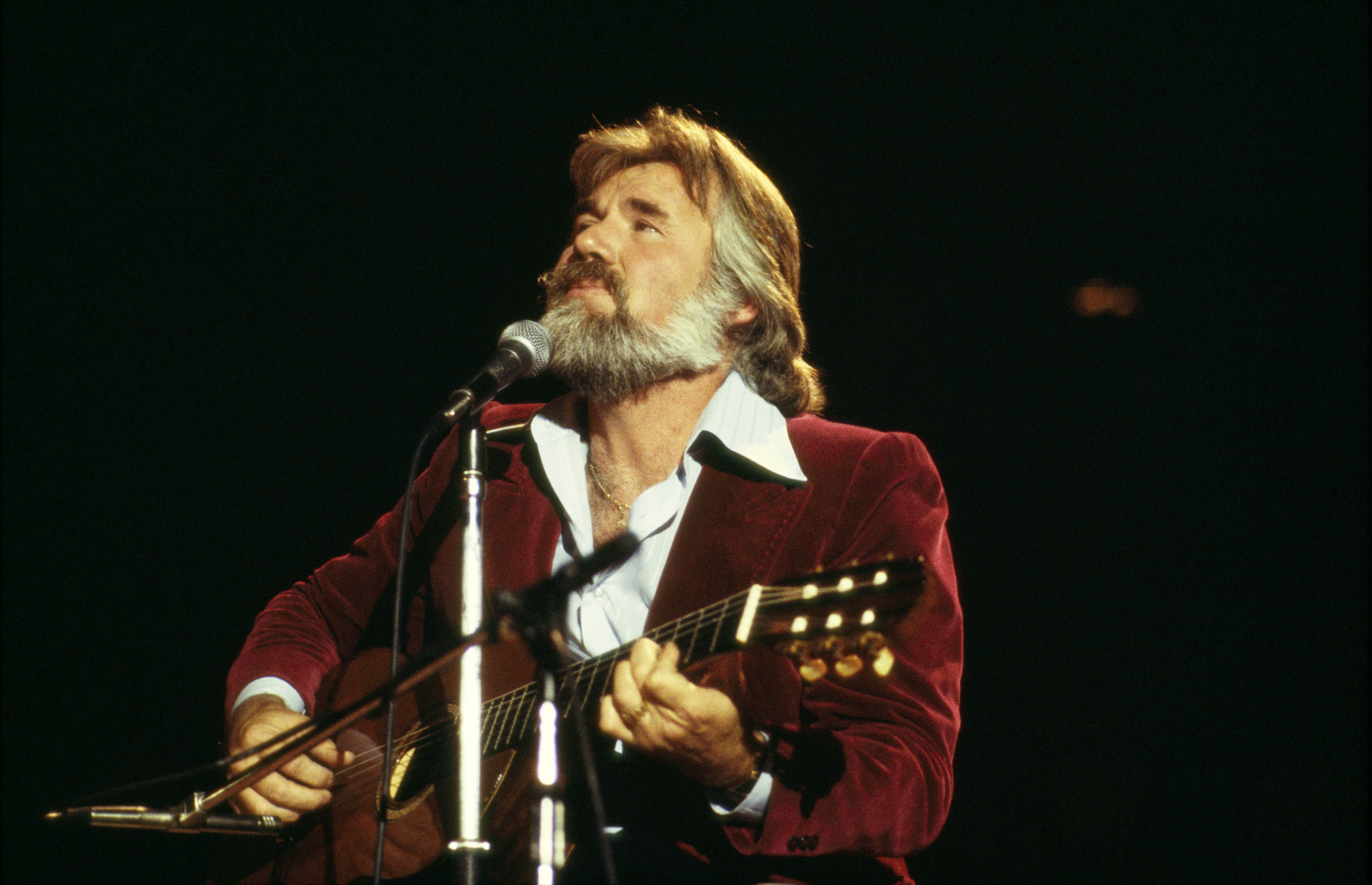 Kenny Rogers wears a red suit and plays the guitar in 1978.