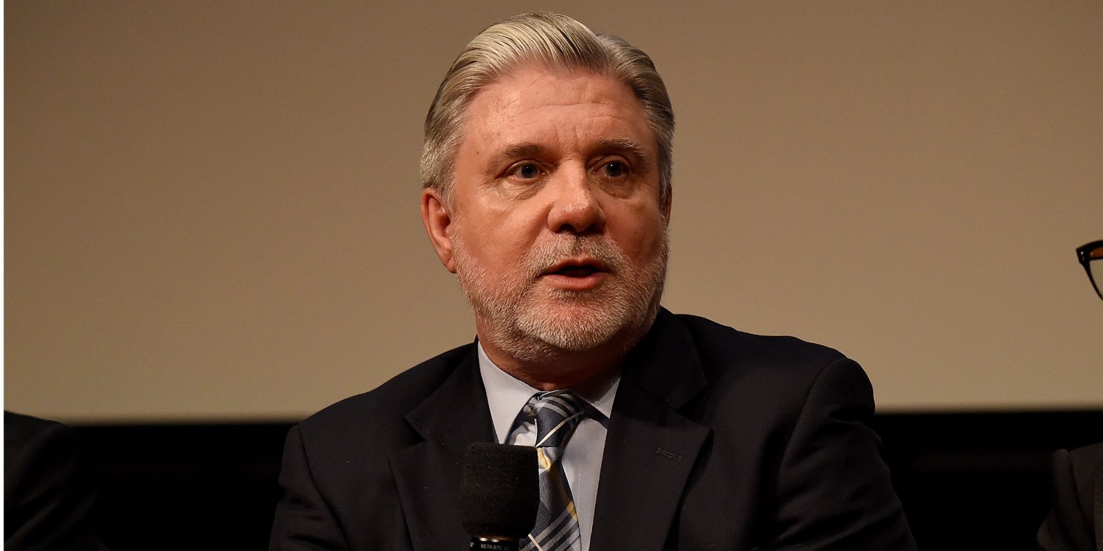 Mike Rinder holds a microphone in a panel discussion regarding Scientology.