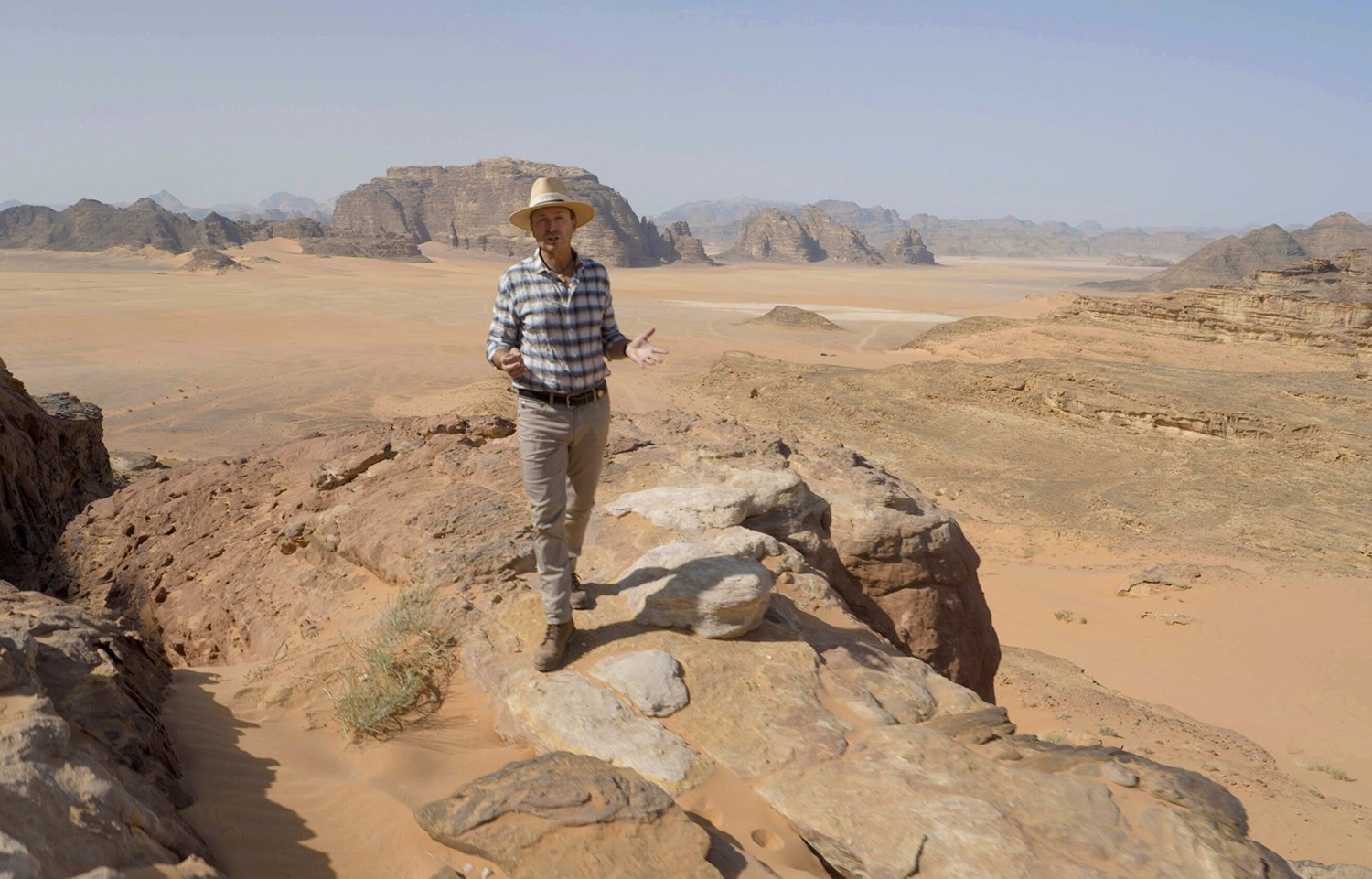 The Amazing Race host Phil Keoghan stands on a rock in the desert in Jordan