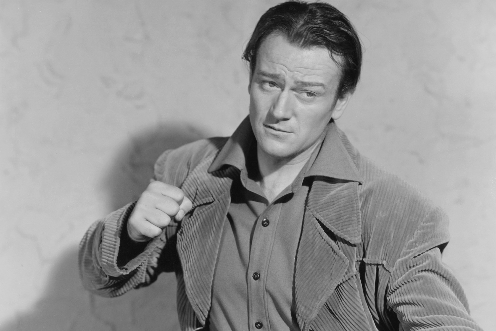Actor John Wayne, who got in a fight with director Budd Boetticher. A black-and-white picture with him holding up his fist, wearing a button-up shirt under a jacket.
