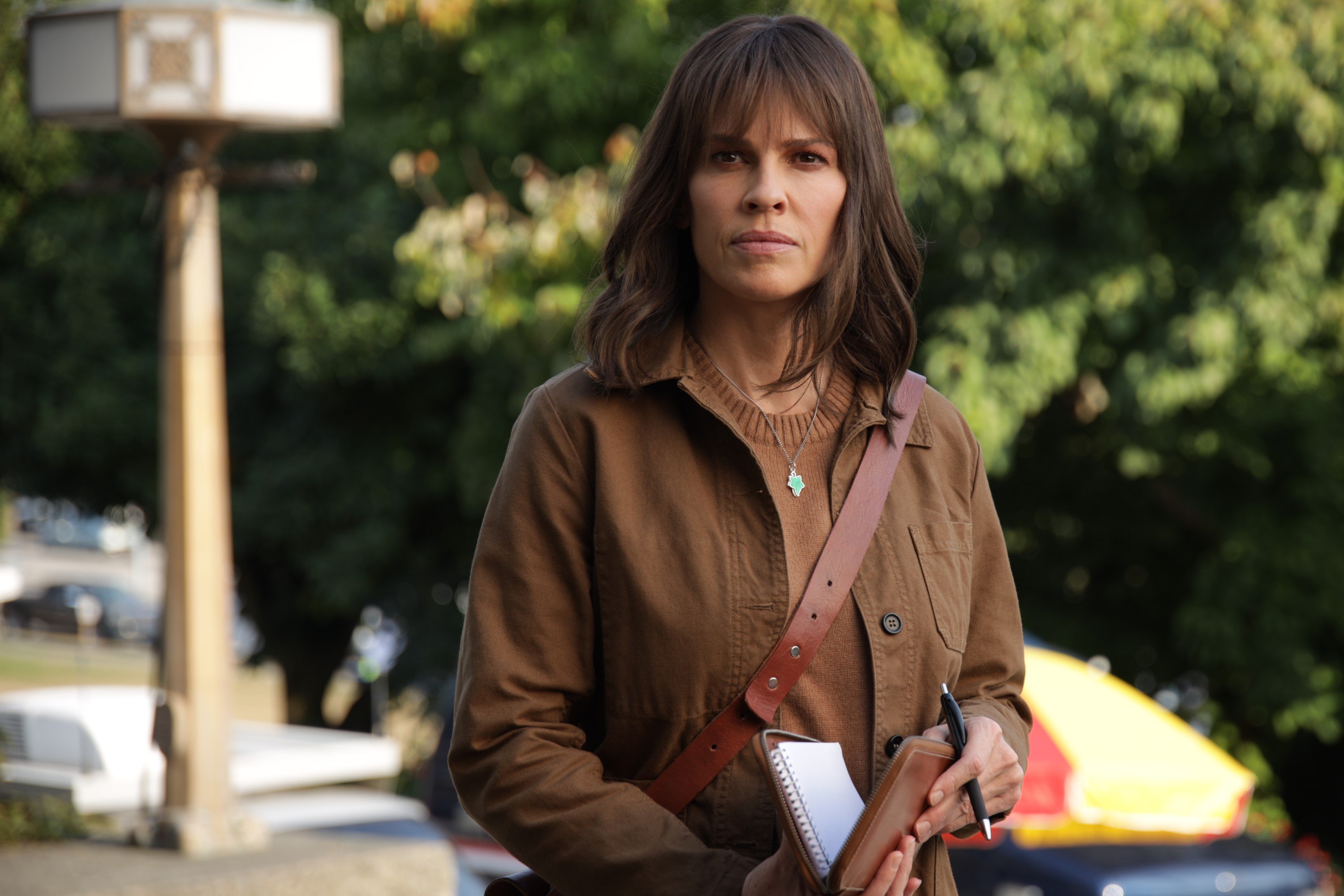 Hilary Swank, in character as Eileen Fitzgerald in 'Alaska Daily' Episode 6 on ABC, wears a brown jacket over a brown sweater and holds a pen and notepad.