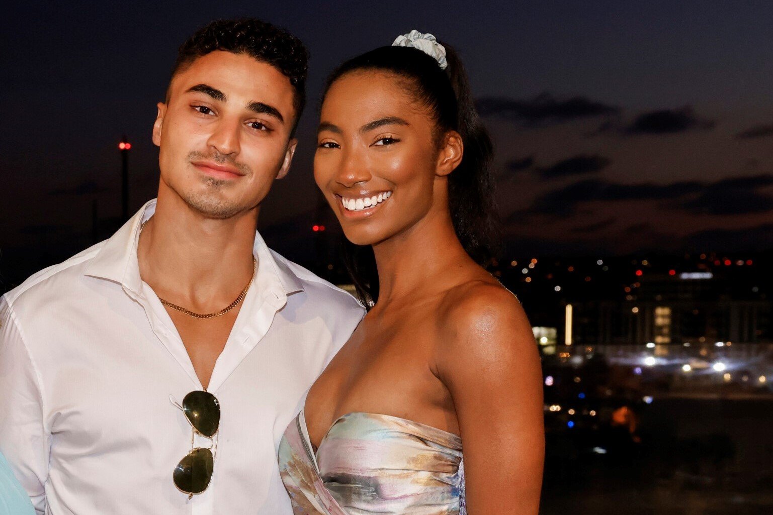 Joseph Abdin and Taylor Hale, who starred in 'Big Brother 24' on CBS, pose for a picture. Joseph wears a white button-up shirt and gold chain. Taylor wears a light pink, blue, and brown strapless dress.
