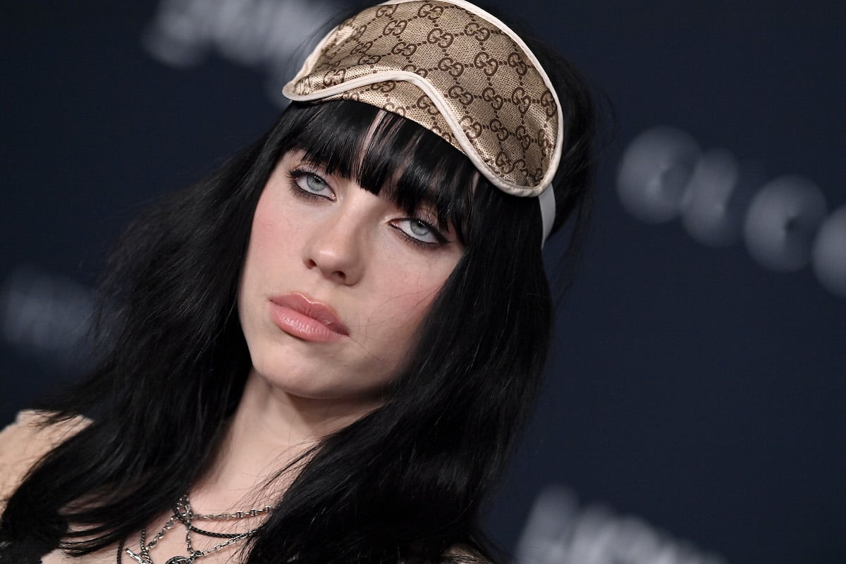 Billie Eilish, who says she has never smoked "weed," poses unsmiling with a sleep mask on her head at an event.