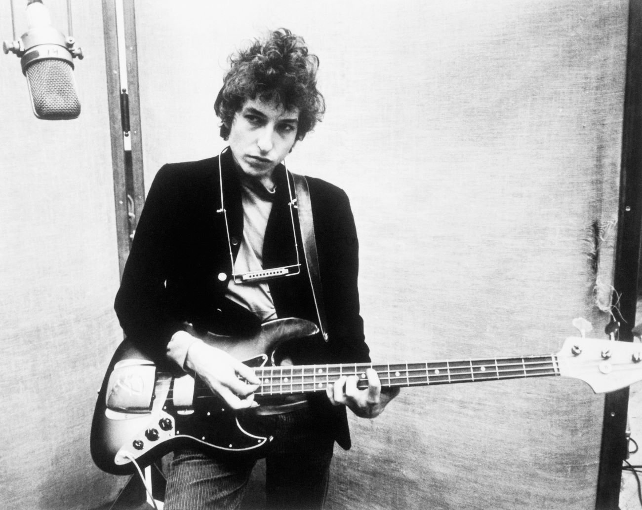 A black and white picture of Bob Dylan holding a guitar.