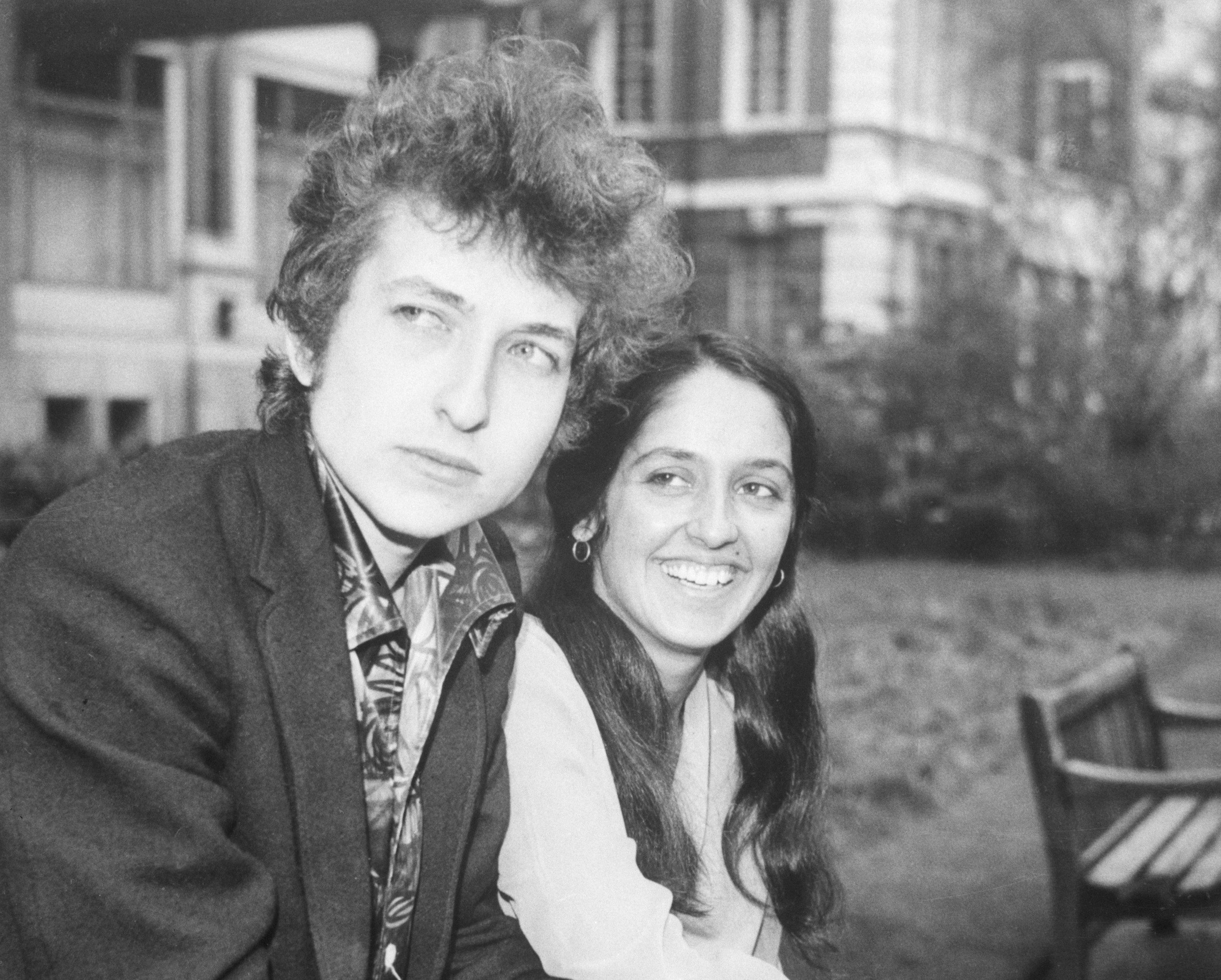 A black and white picture of Bob Dylan and Joan Baez sitting on a bench together. 