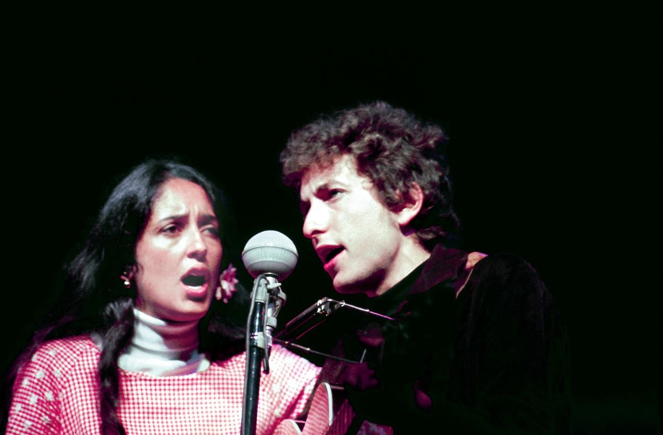 Joan Baez and Bob Dylan sing into a microphone together.