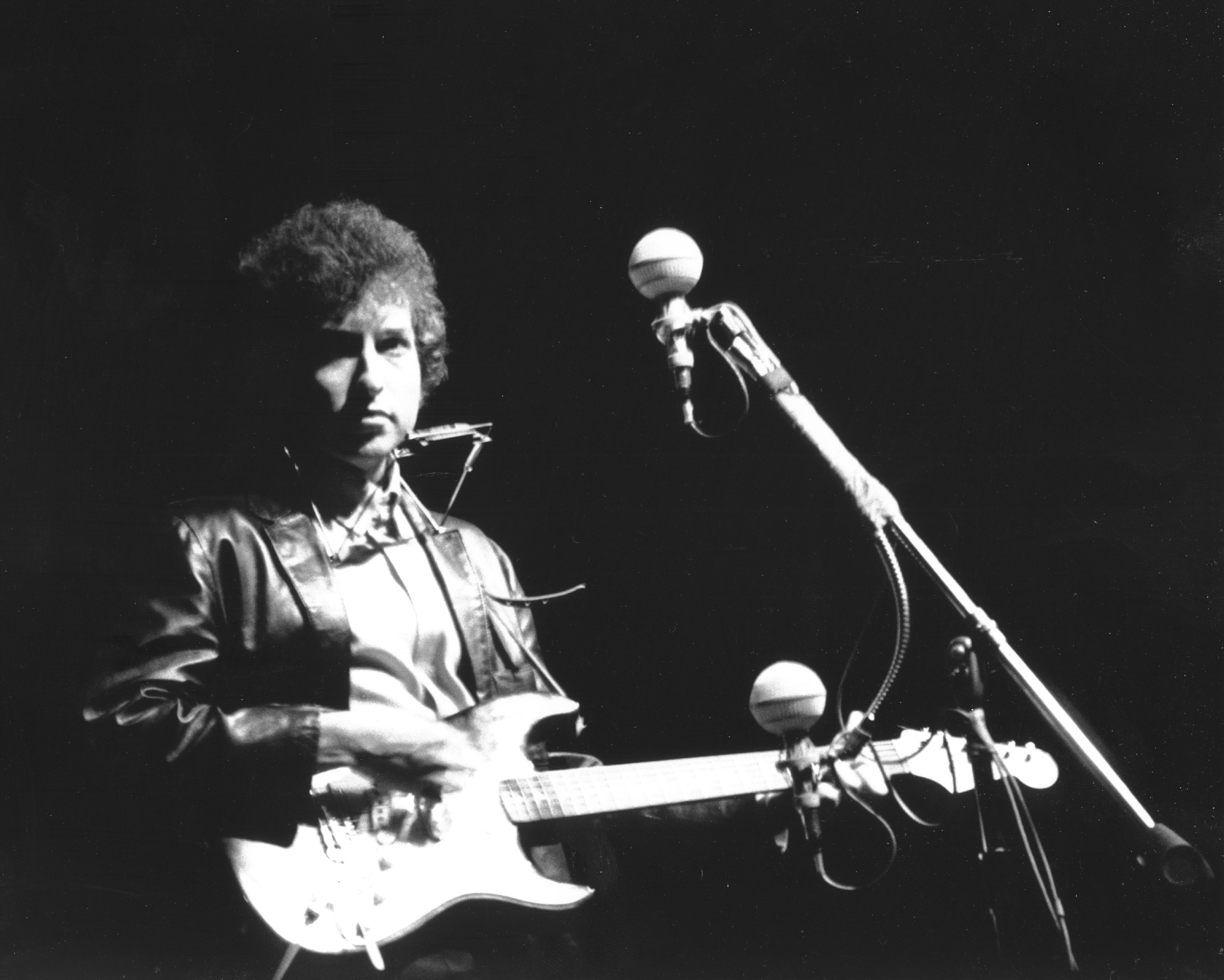 A black and white picture of Bob Dylan holding an electric guitar at the Newport Folk Festival.