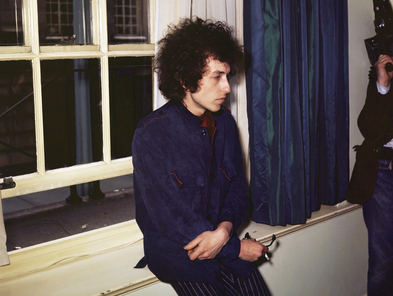 Bob Dylan leans on a window ledge and holds a cigarette.