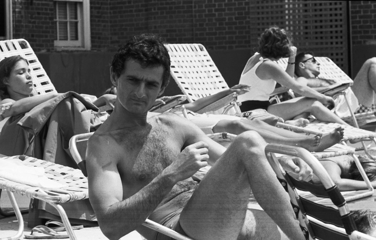 A black and white picture of Bob Dylan's tour manager Victor Maymudes sitting on a deck chair in a bathing suit.