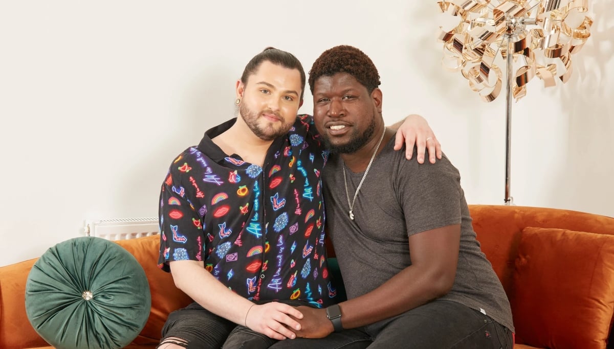 Calum and Marvin holding hands and sitting on the couch together for '90 Day Fiancé UK' Season 1 on discovery+.