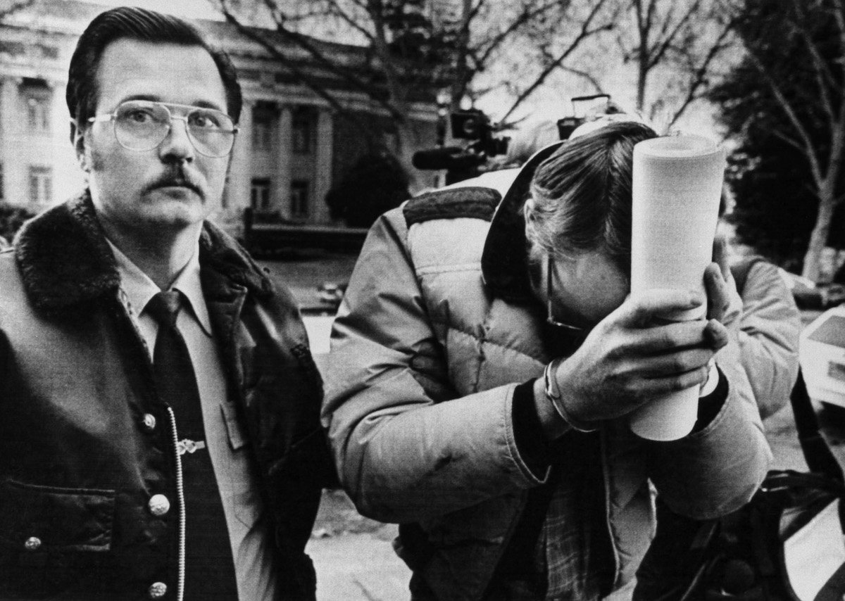 Cameron Hooker, hiding his face, being escorted by a police officer