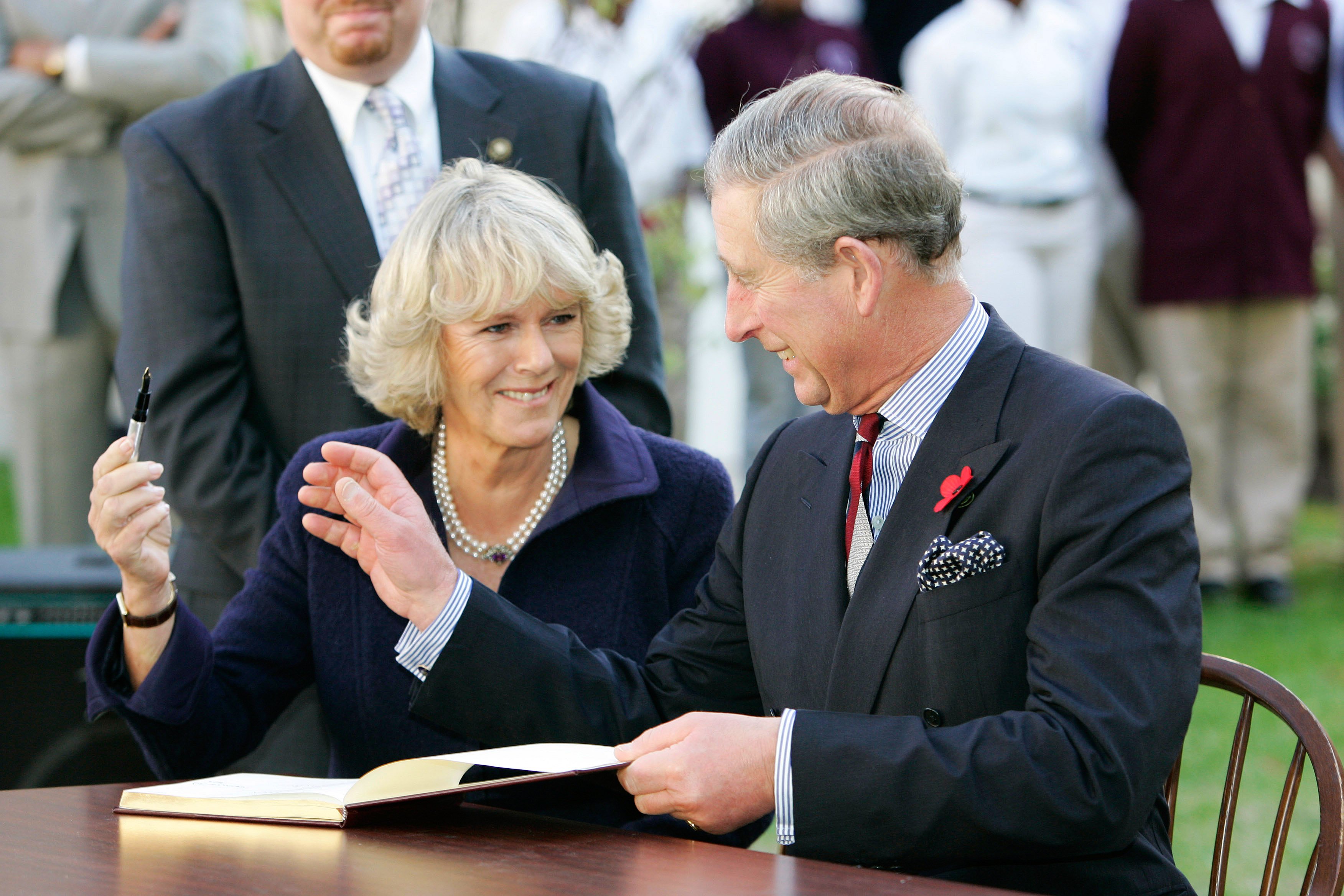 Camilla Parker Bowles and King Charles III giggle and joke with each other while signing the visitors' book at SEED School