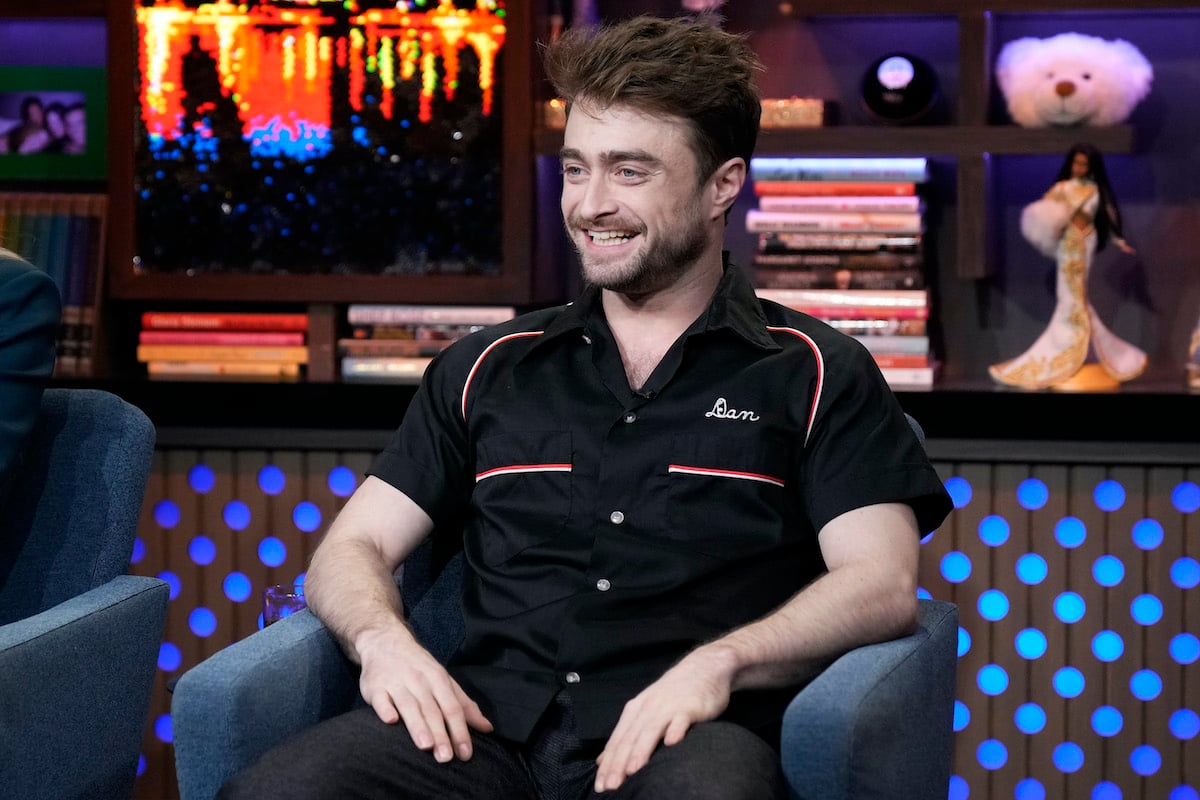 Daniel Radcliffe star of the Harry Potter movies smiles in all black whilst sitting in a chair