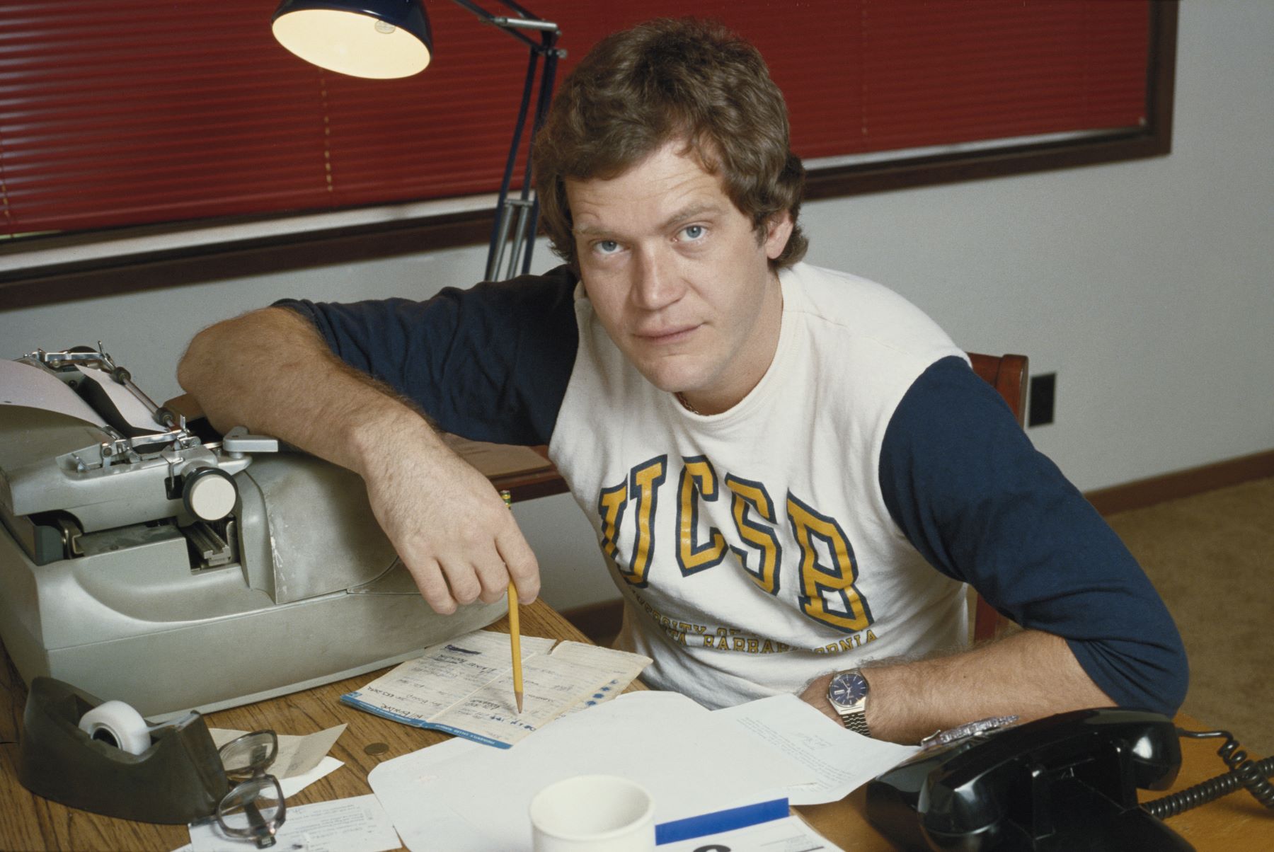 TV show host and comedian David Letterman pictured writing at a desk in 1980